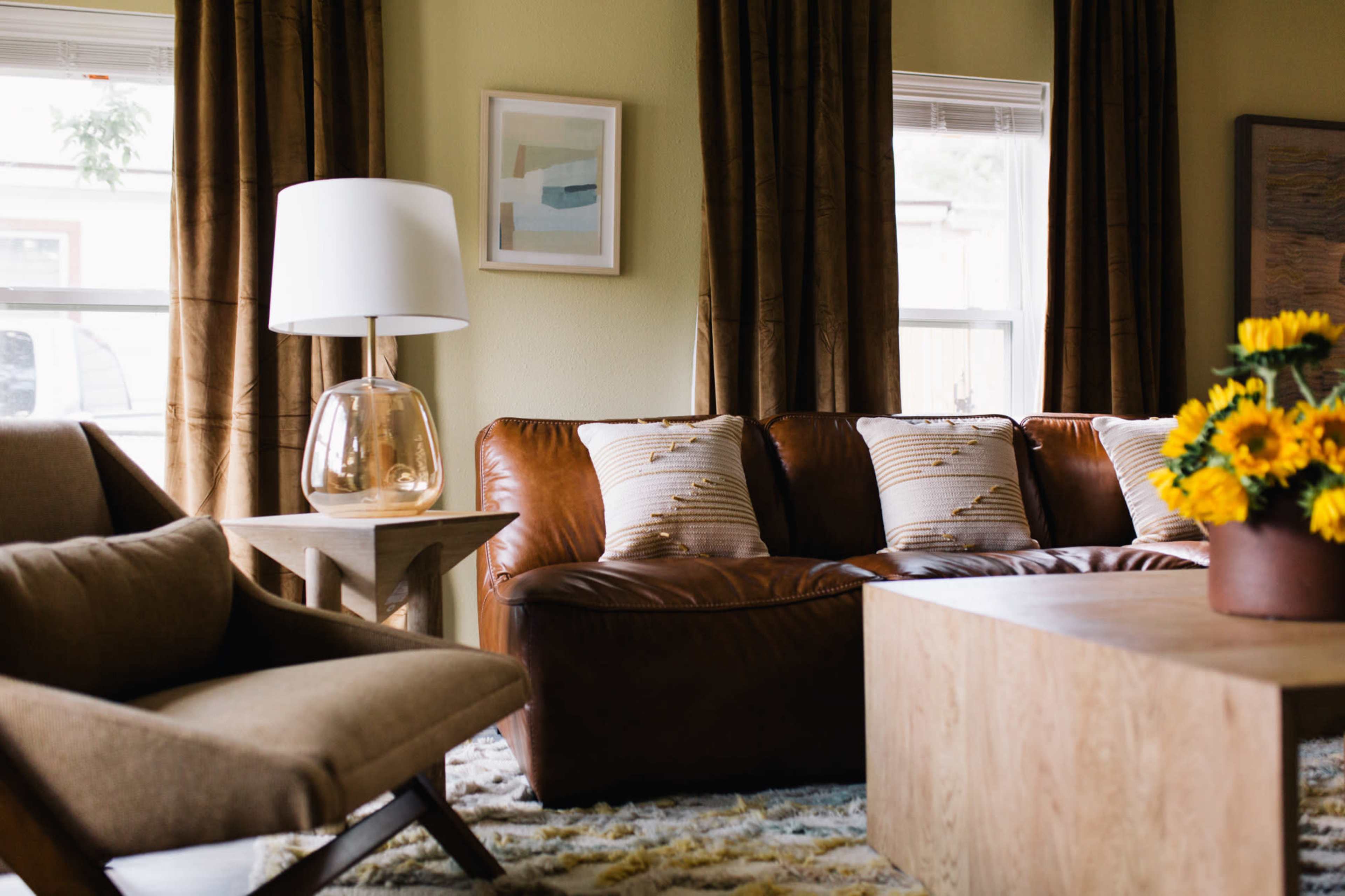 The image shows a living room with a brown leather couch, an armchair, a wooden coffee table, and a vase of sunflowers on the table.