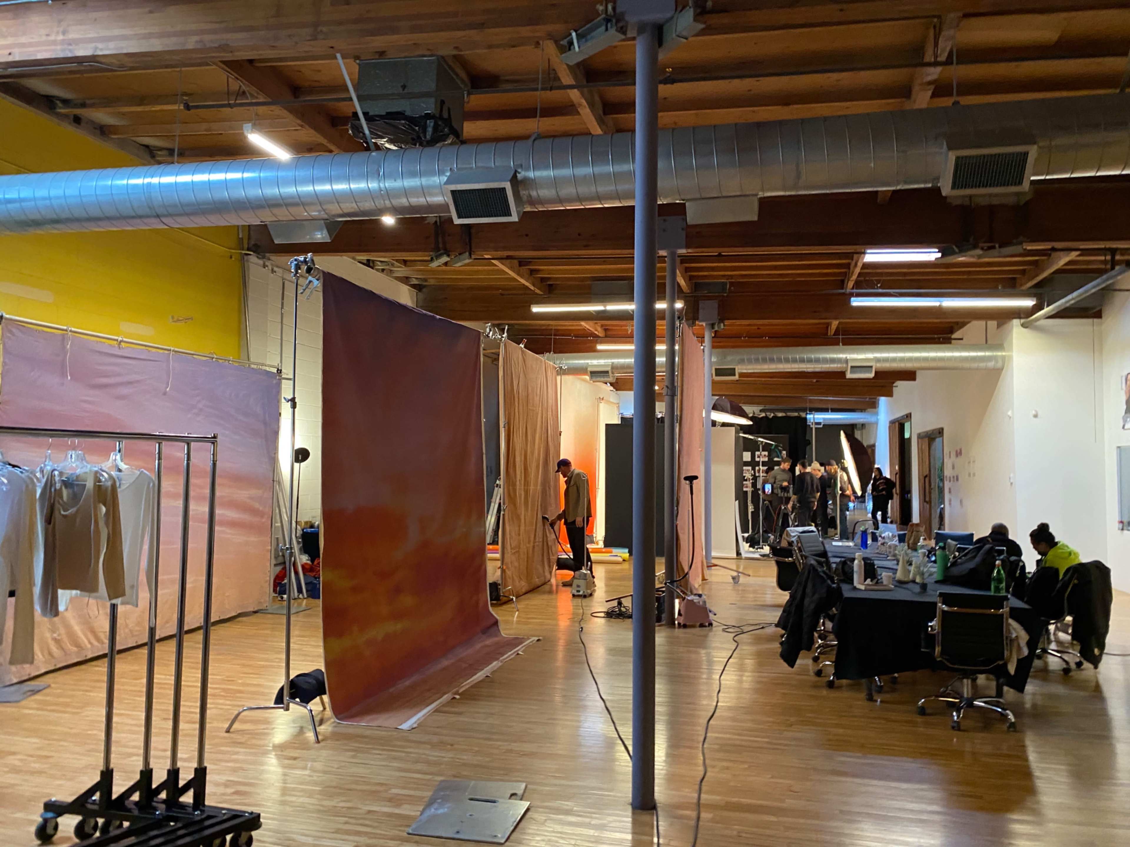 The image shows a spacious studio with various backdrops set up for a photo shoot, along with equipment and clothing racks on display.