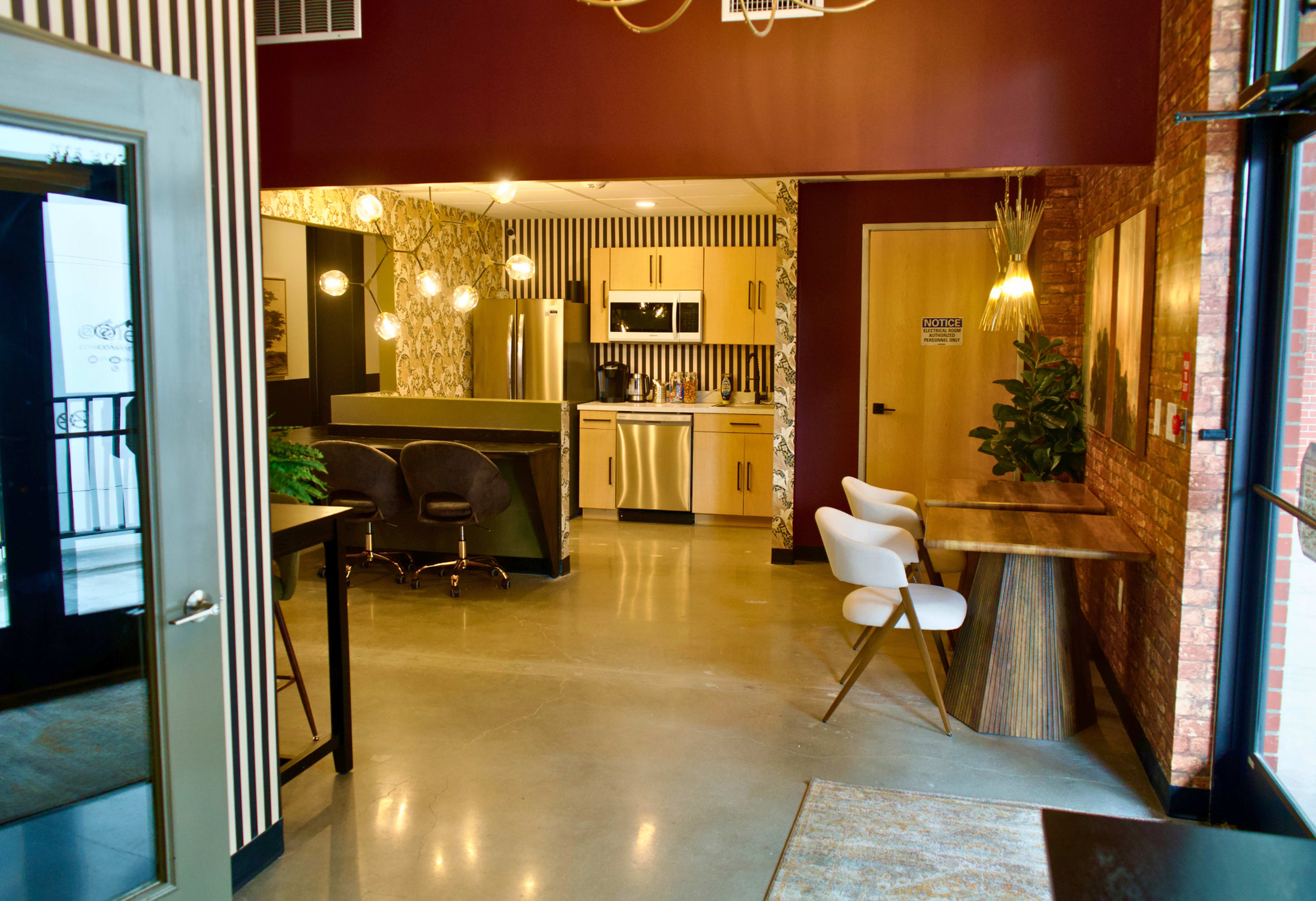 The image shows a modern interior space with a kitchen area, seating arrangements, and decorative elements.
