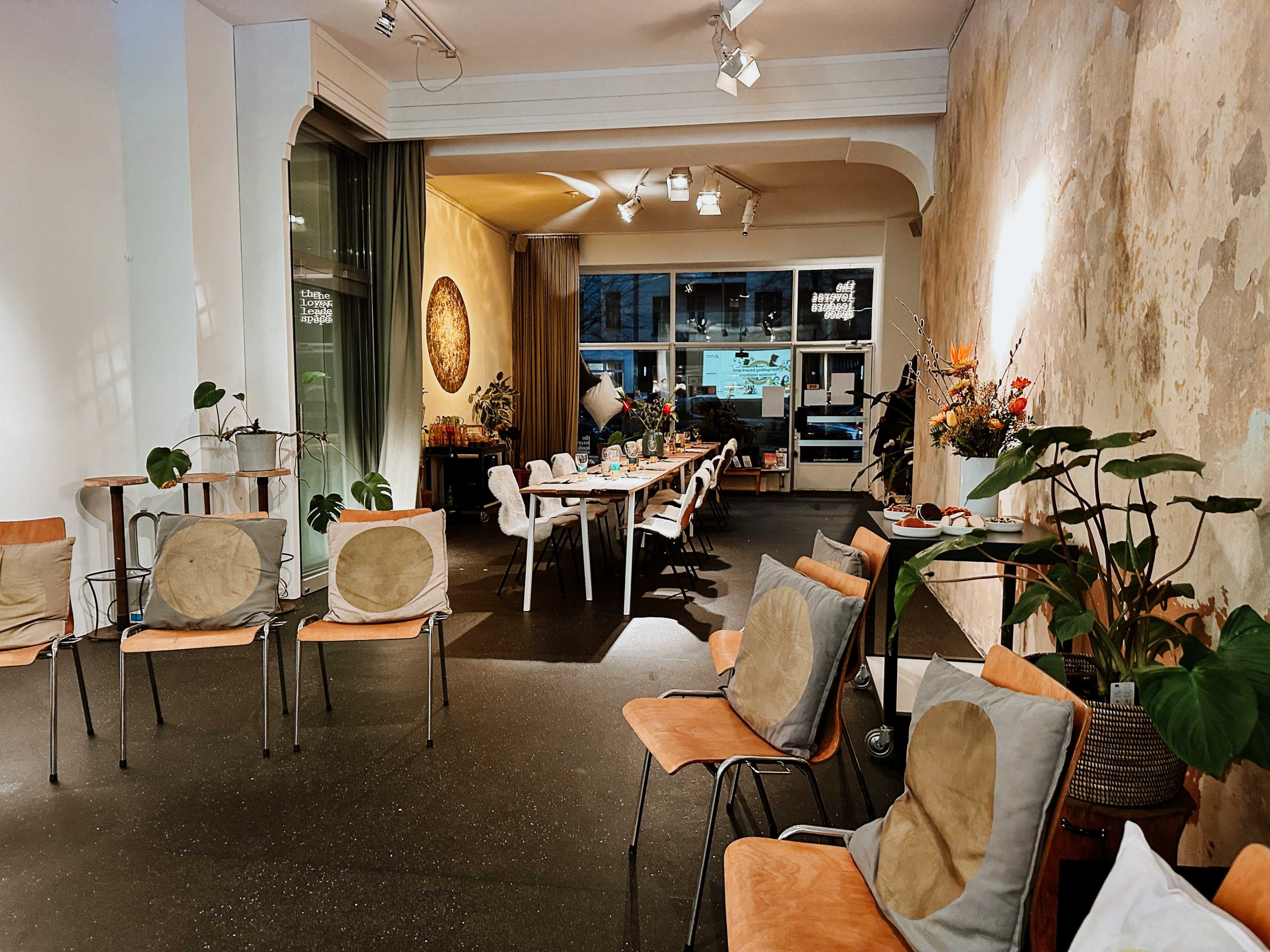 A spacious interior with a long dining table, surrounded by chairs, and adorned with plants against a backdrop of textured wall.
