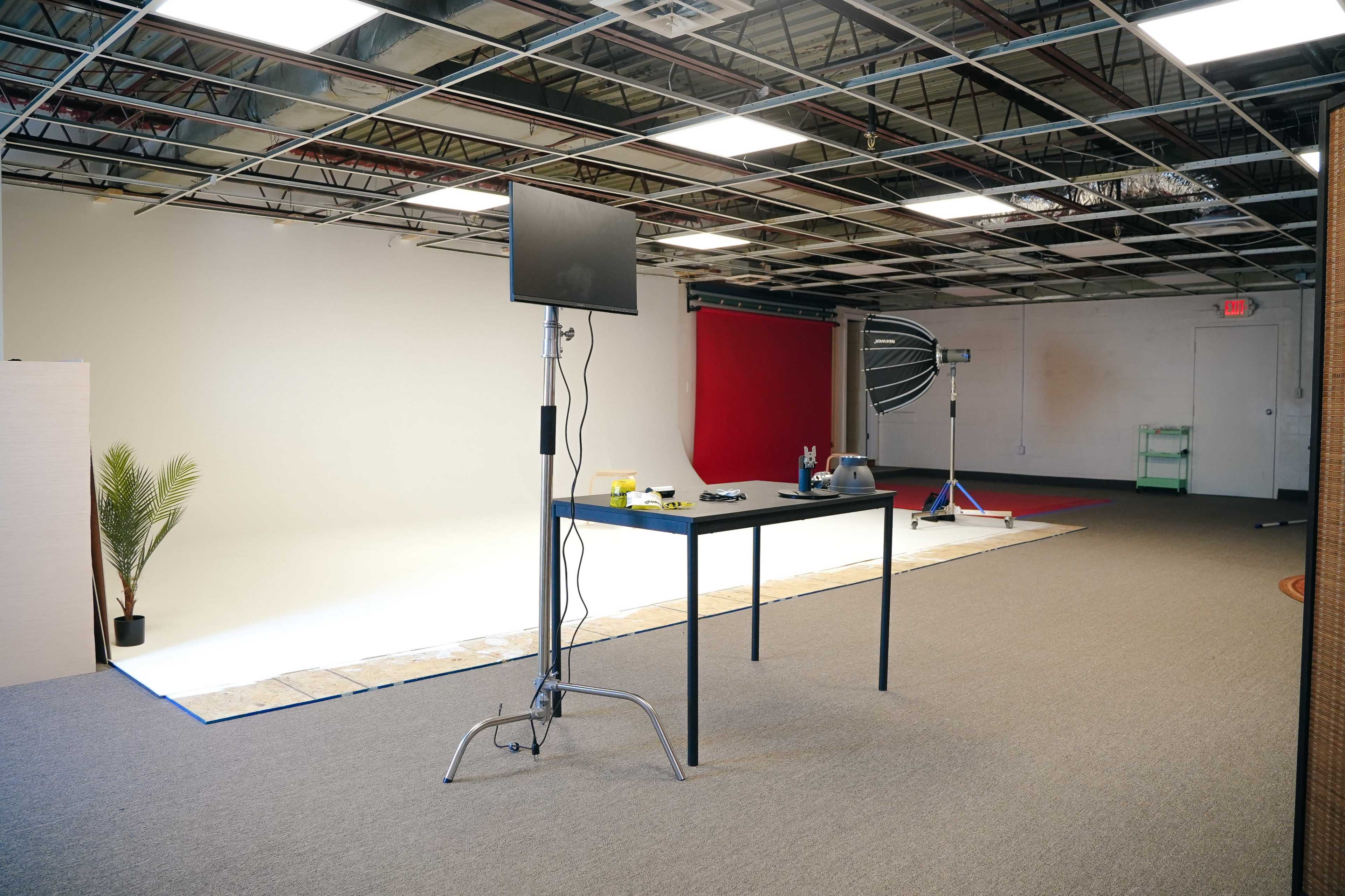 A photography studio features a table with equipment and a backdrop, with sections of white and red walls visible.