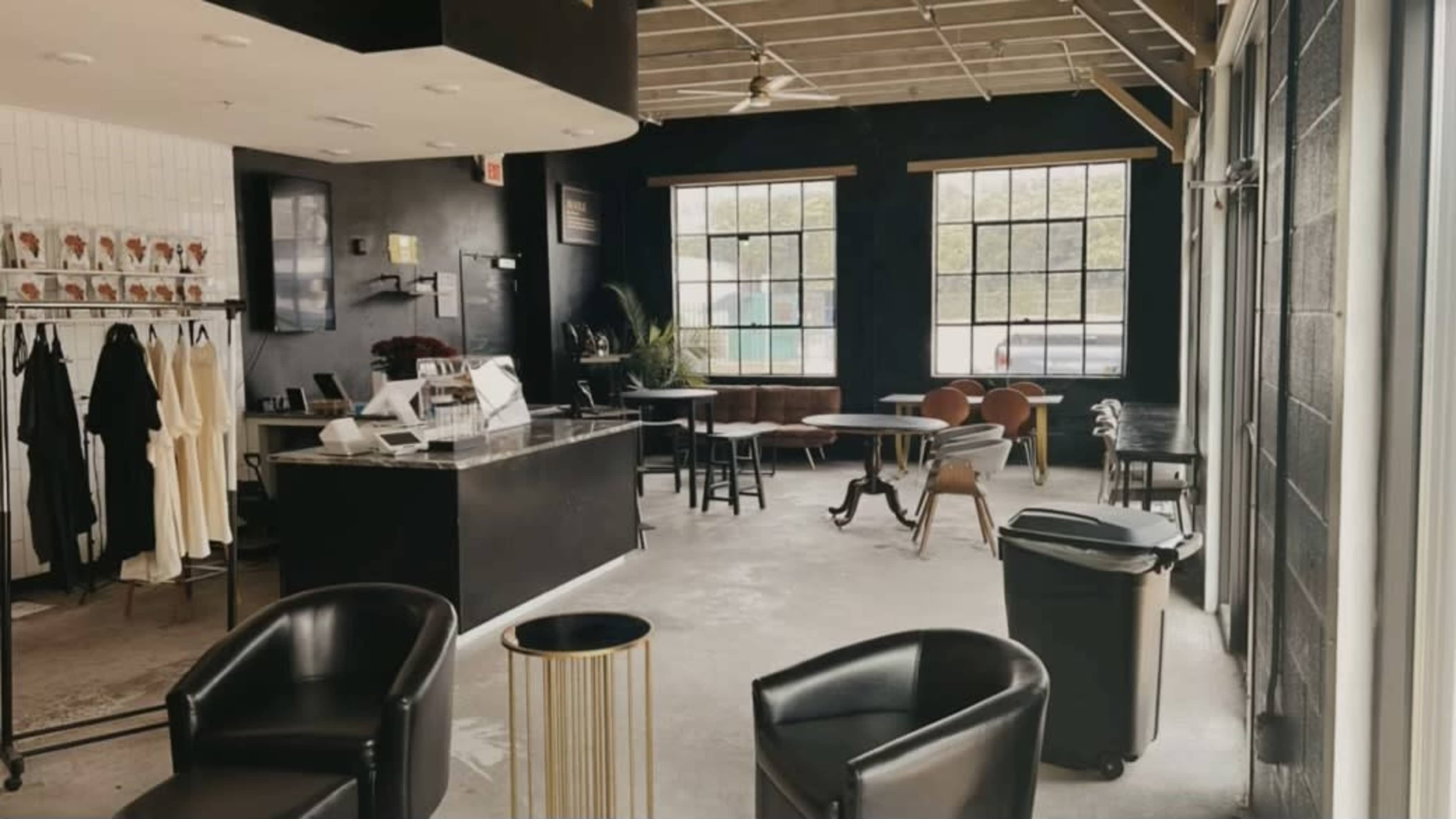 A modern interior of a café or retail space featuring a counter, seating areas with various chairs, and large windows allowing natural light.