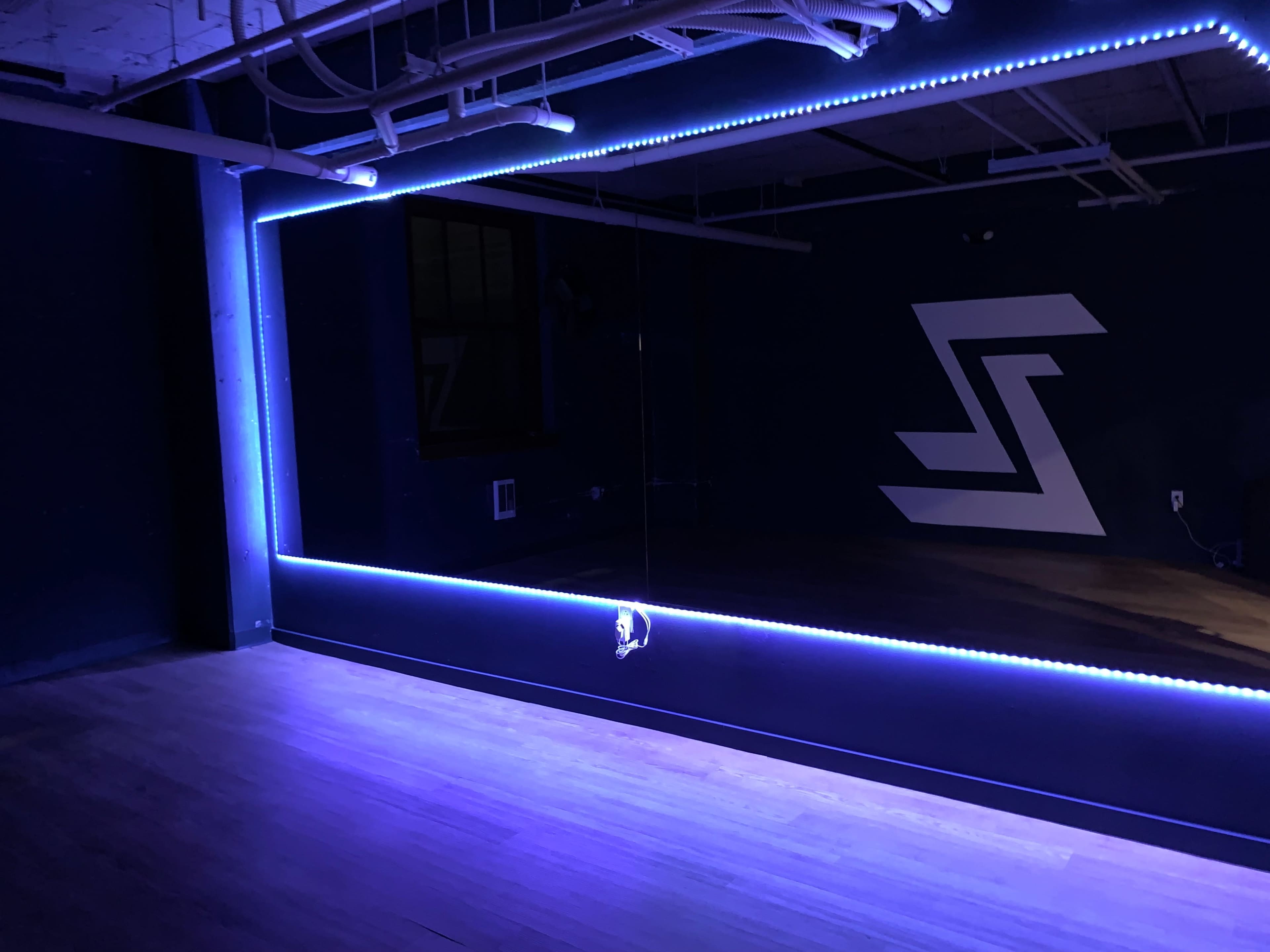 The image shows a dimly lit room with a large mirror framed by blue LED lights and a geometric design on the wall.