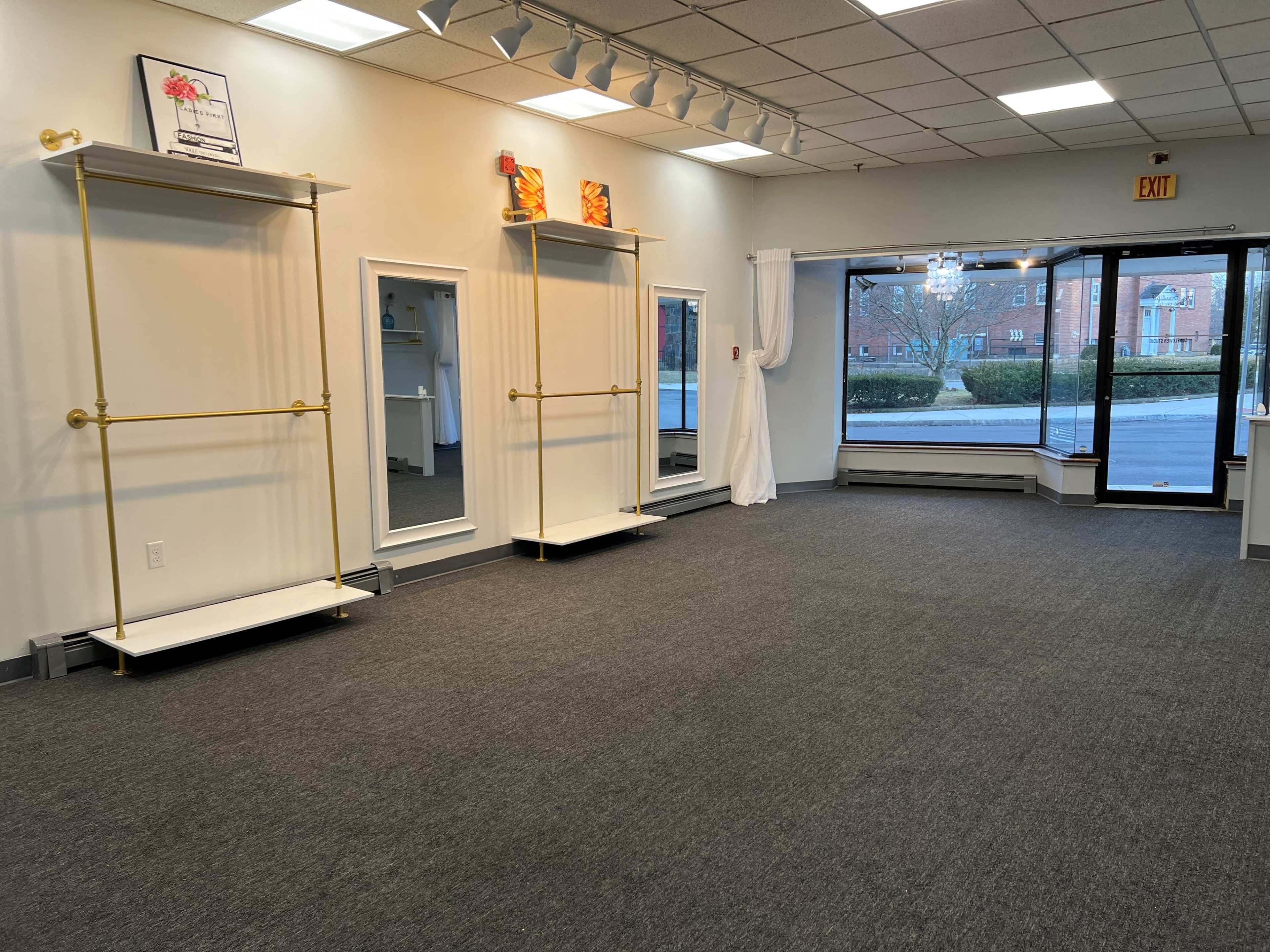 An empty retail space with two gold display racks and large windows facing a street, along with a separate entrance area.