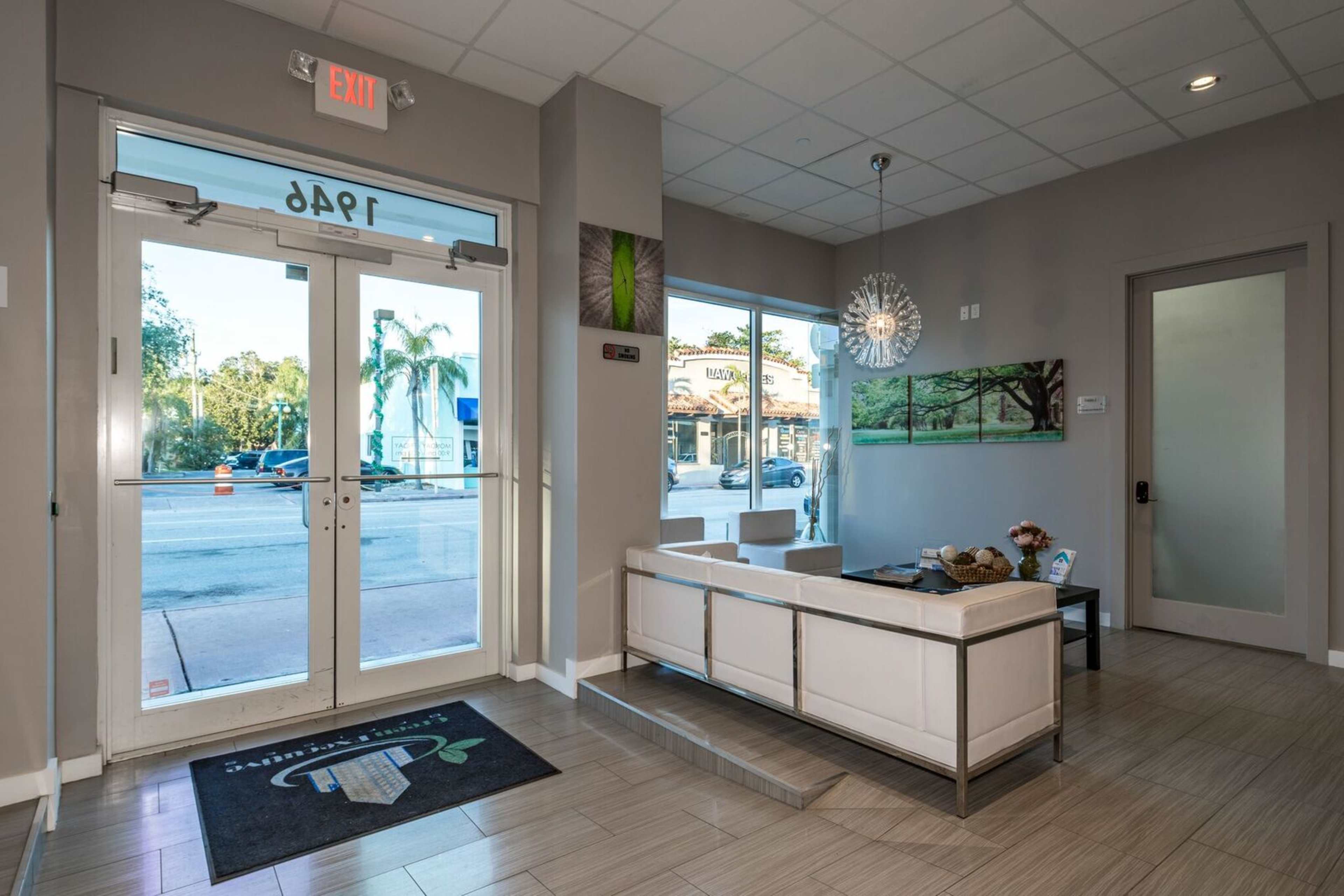 The image shows a modern reception area with a white seating arrangement and large windows facing a street.