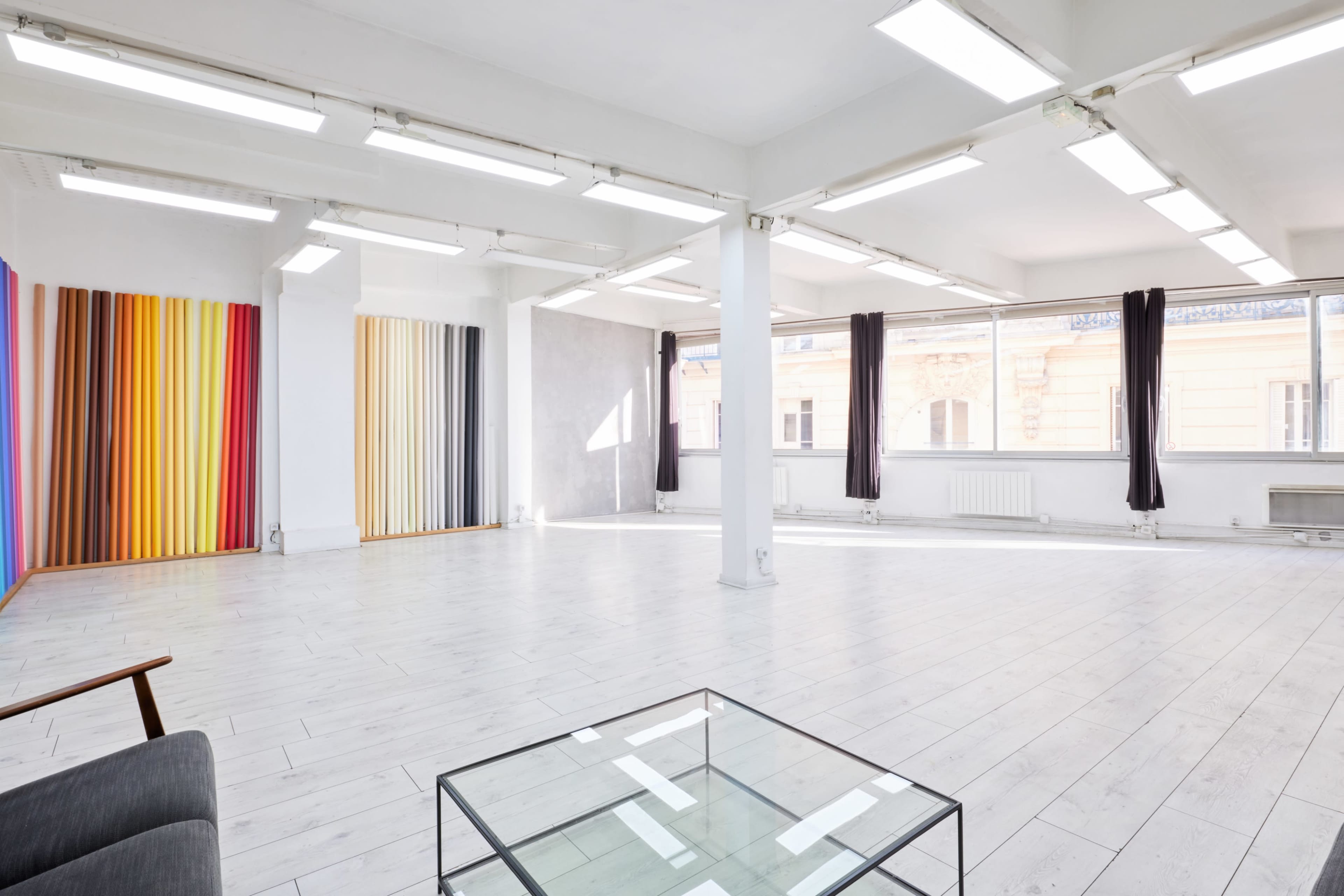 The image shows a spacious, well-lit studio with white walls, wooden flooring, and color-striped artwork on one side.