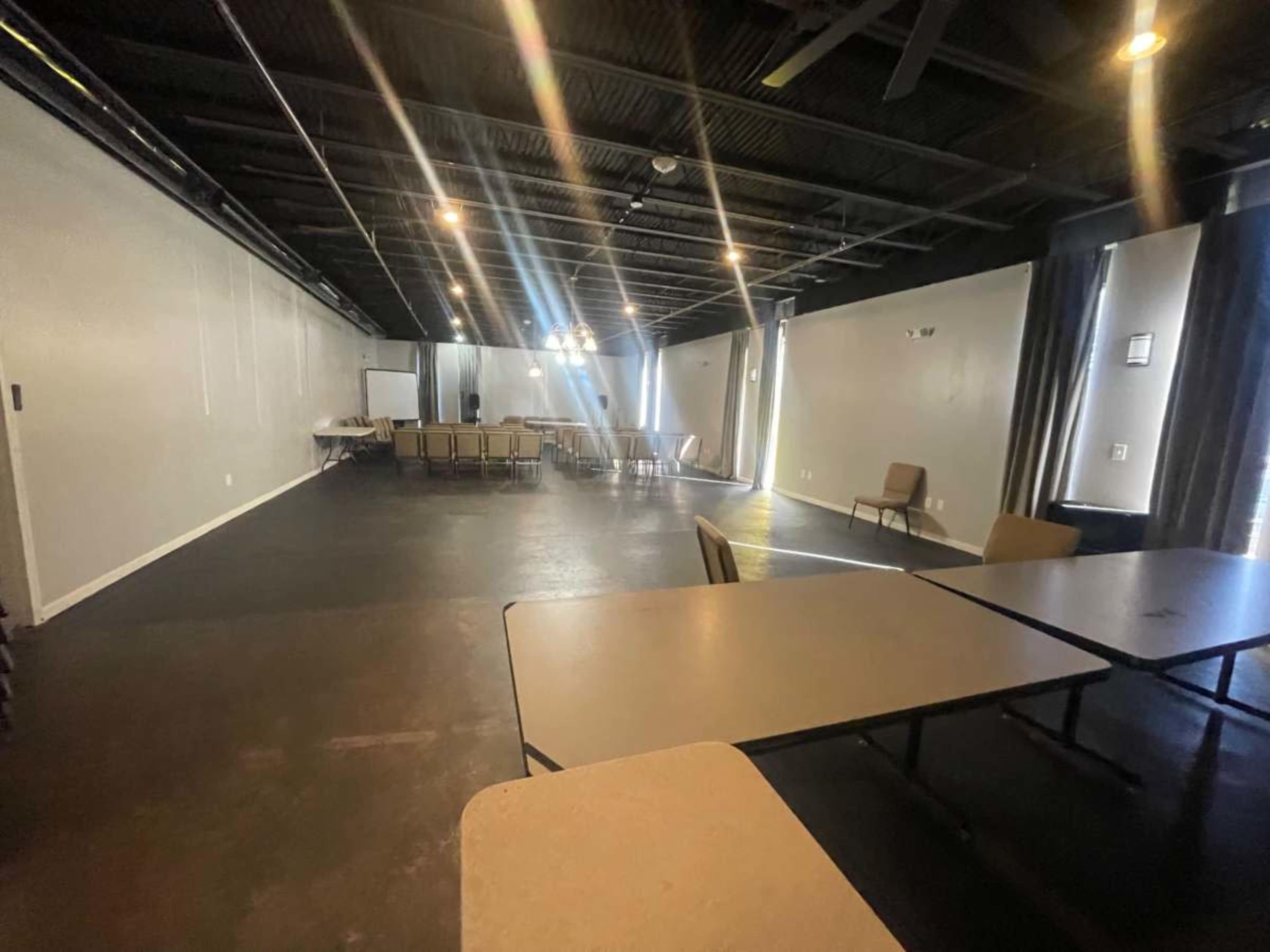 The image shows an empty meeting room with tables and chairs arranged in a professional setting.