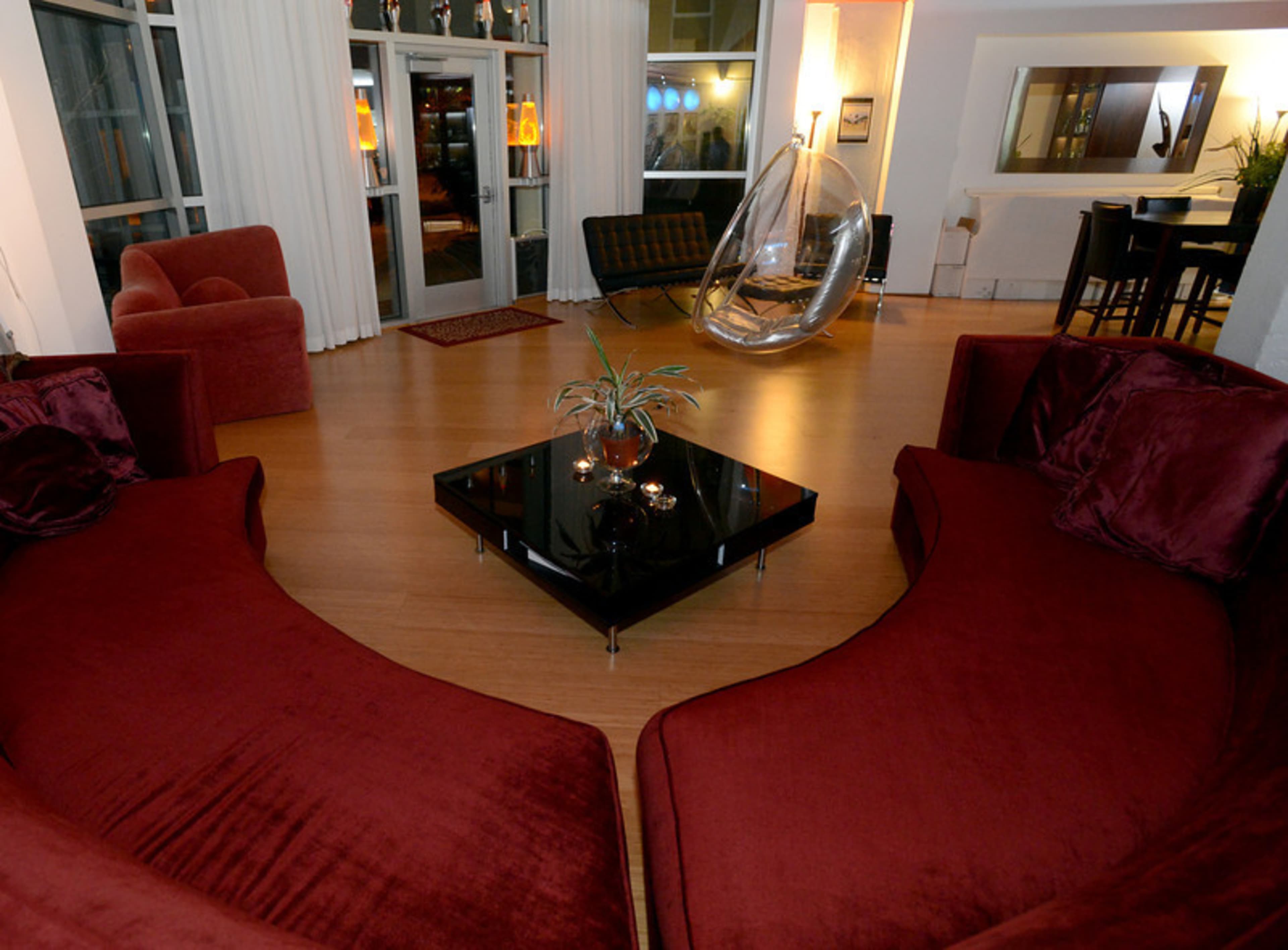A modern living room with a dark coffee table surrounded by red curved sofas and a transparent egg-shaped chair.