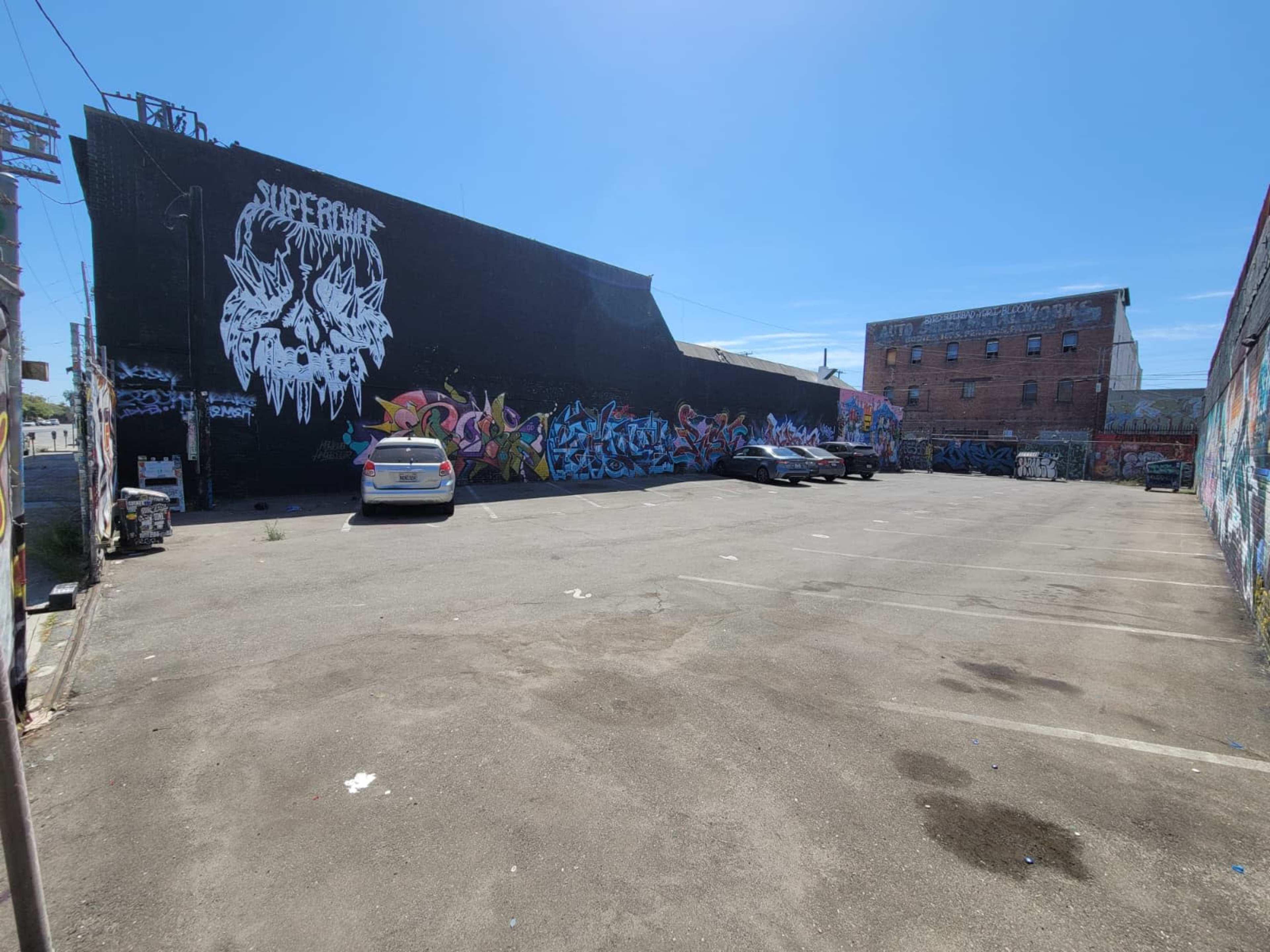 The image shows an empty parking lot with a large wall covered in colorful graffiti art and two parked cars.