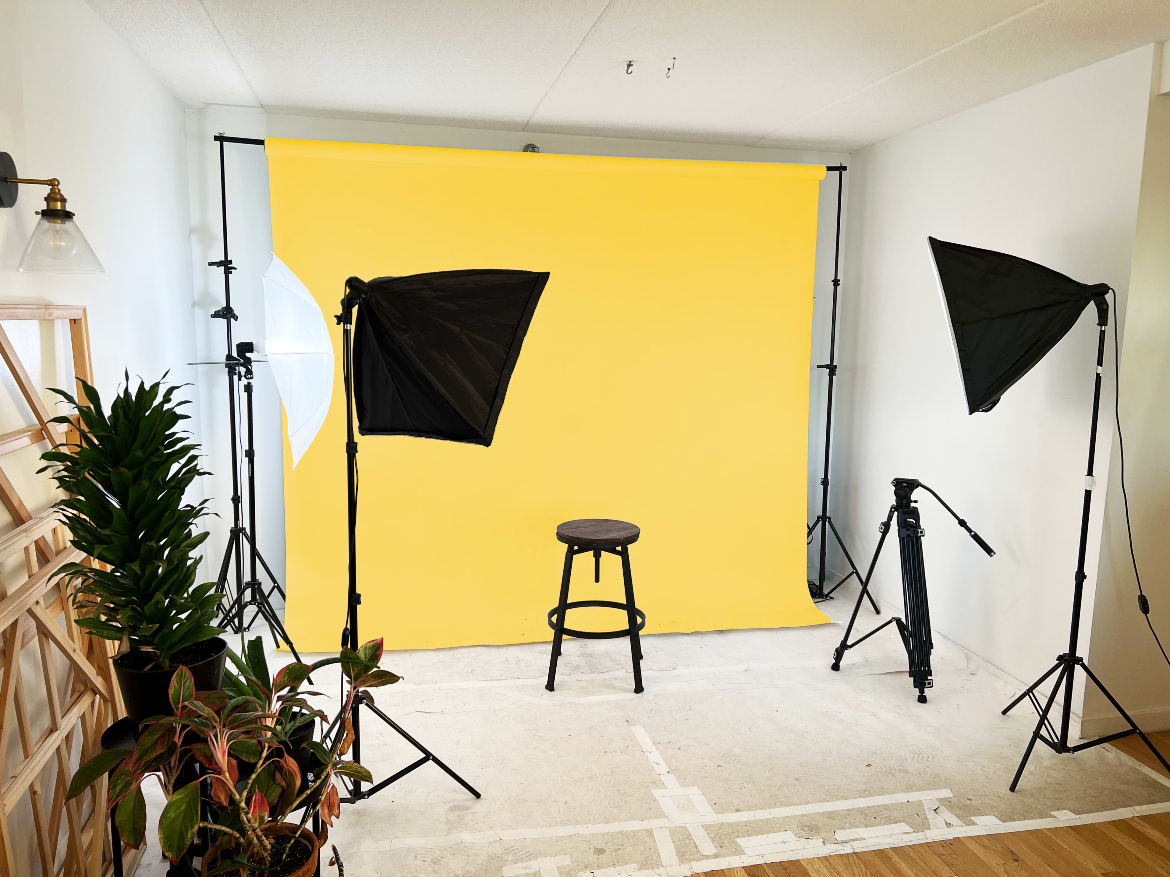 A photography studio setup featuring a yellow backdrop, a black stool in the center, and studio lighting equipment on either side.