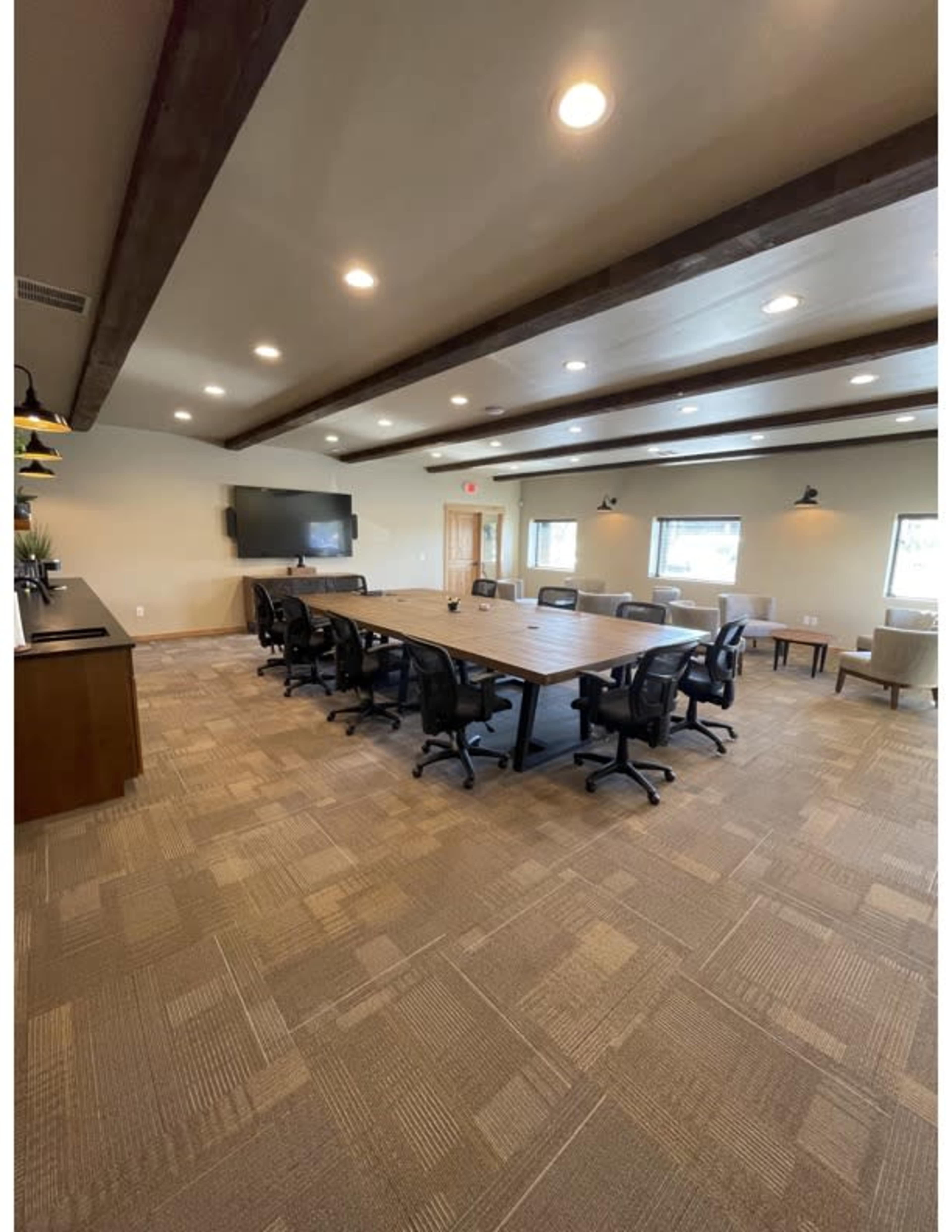 A spacious conference room features a large table surrounded by swivel chairs, a wall-mounted television, and large windows.