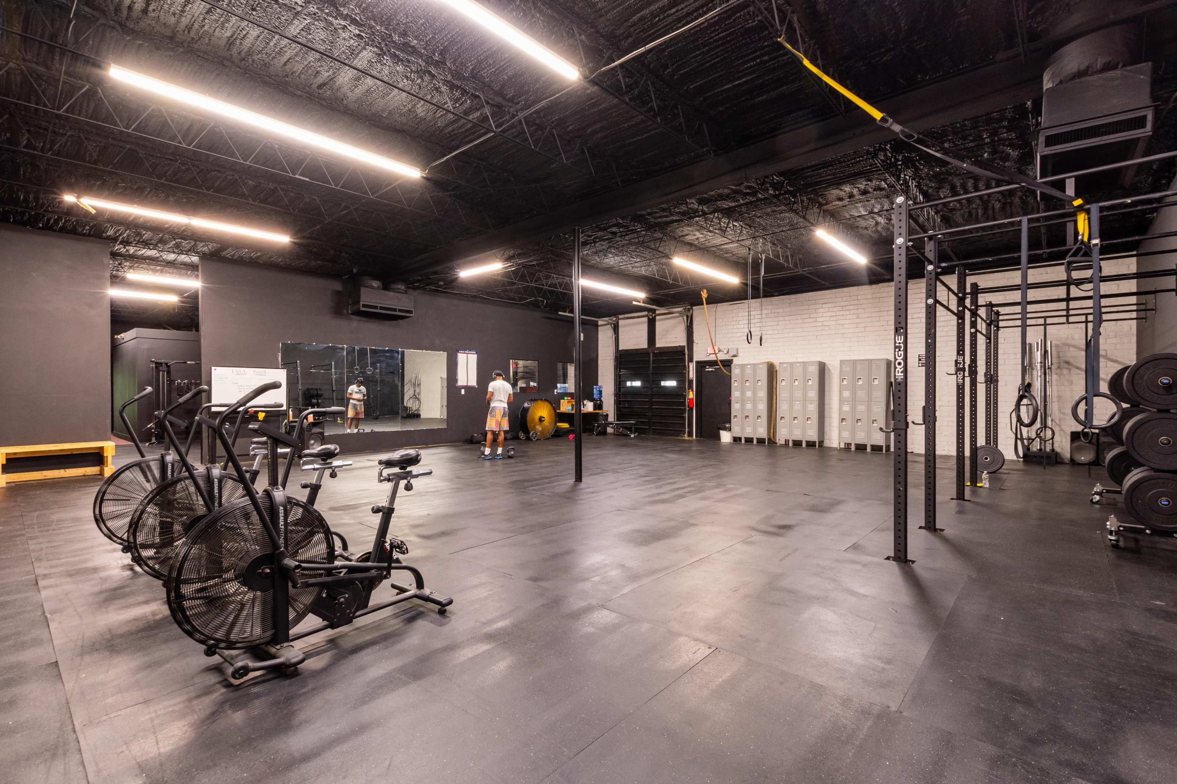 A spacious gym features exercise equipment, including stationary bikes, a weight area, and a pull-up bar, with open floor space for workouts.