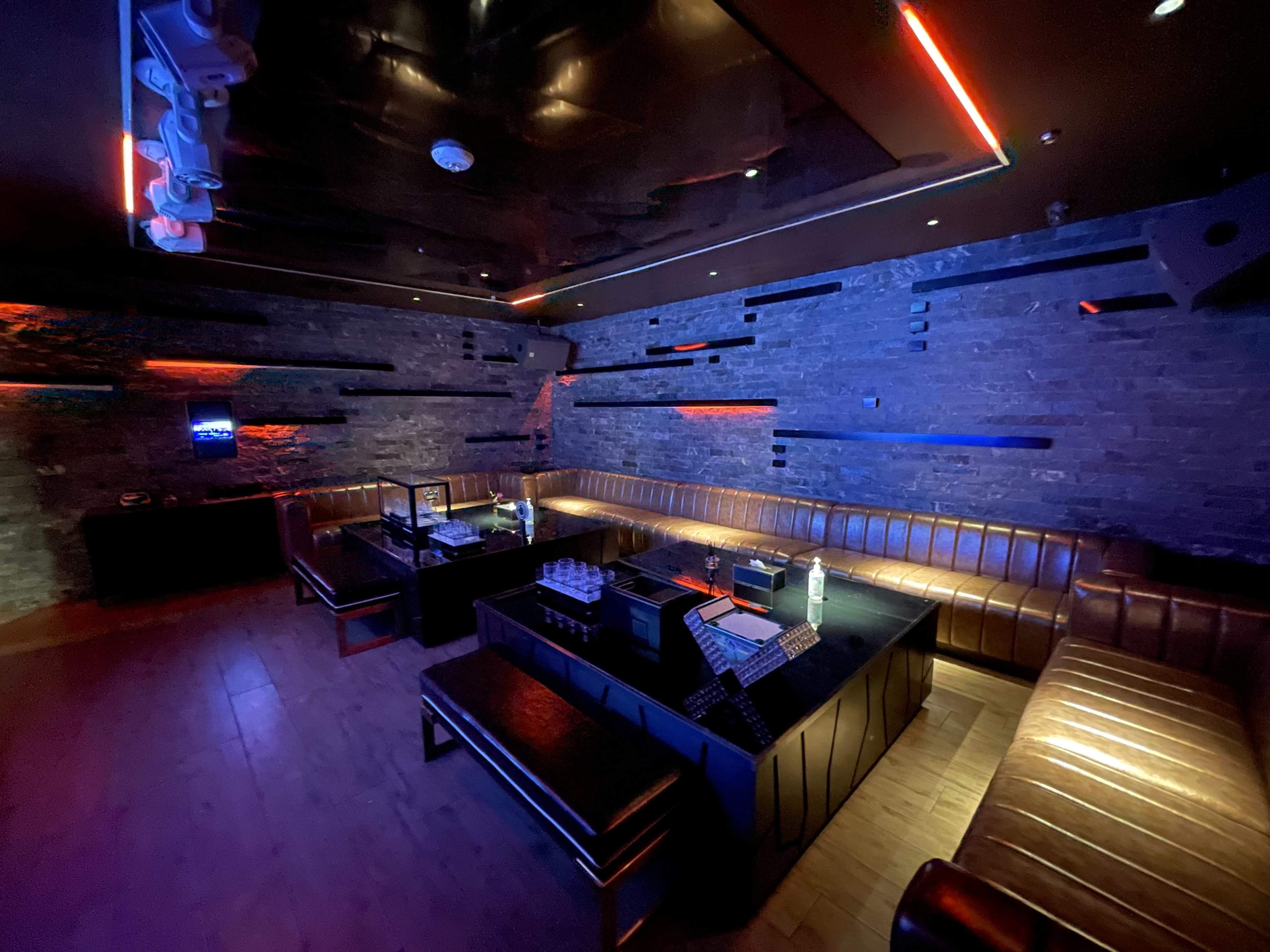 A dimly lit lounge area with leather seating and wooden flooring, featuring a table set up for drinks and a modern, minimalist design.