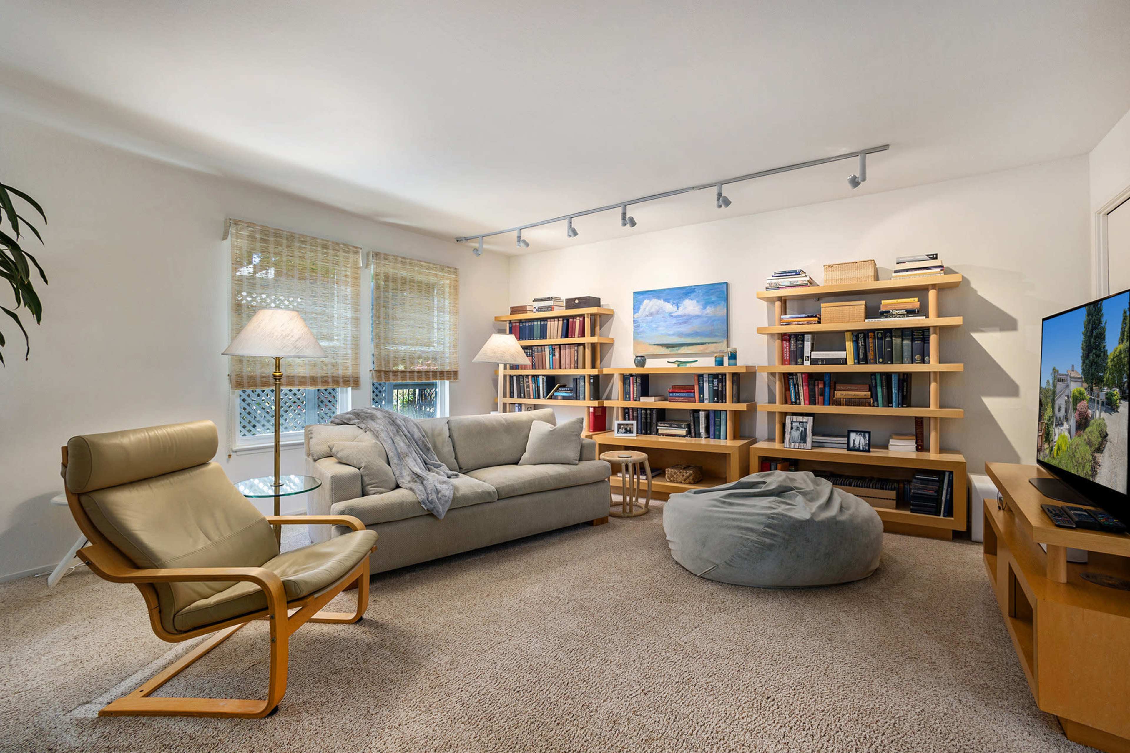 A cozy living room features a sofa, a bean bag chair, a bookshelf filled with books, and a large television against one wall.