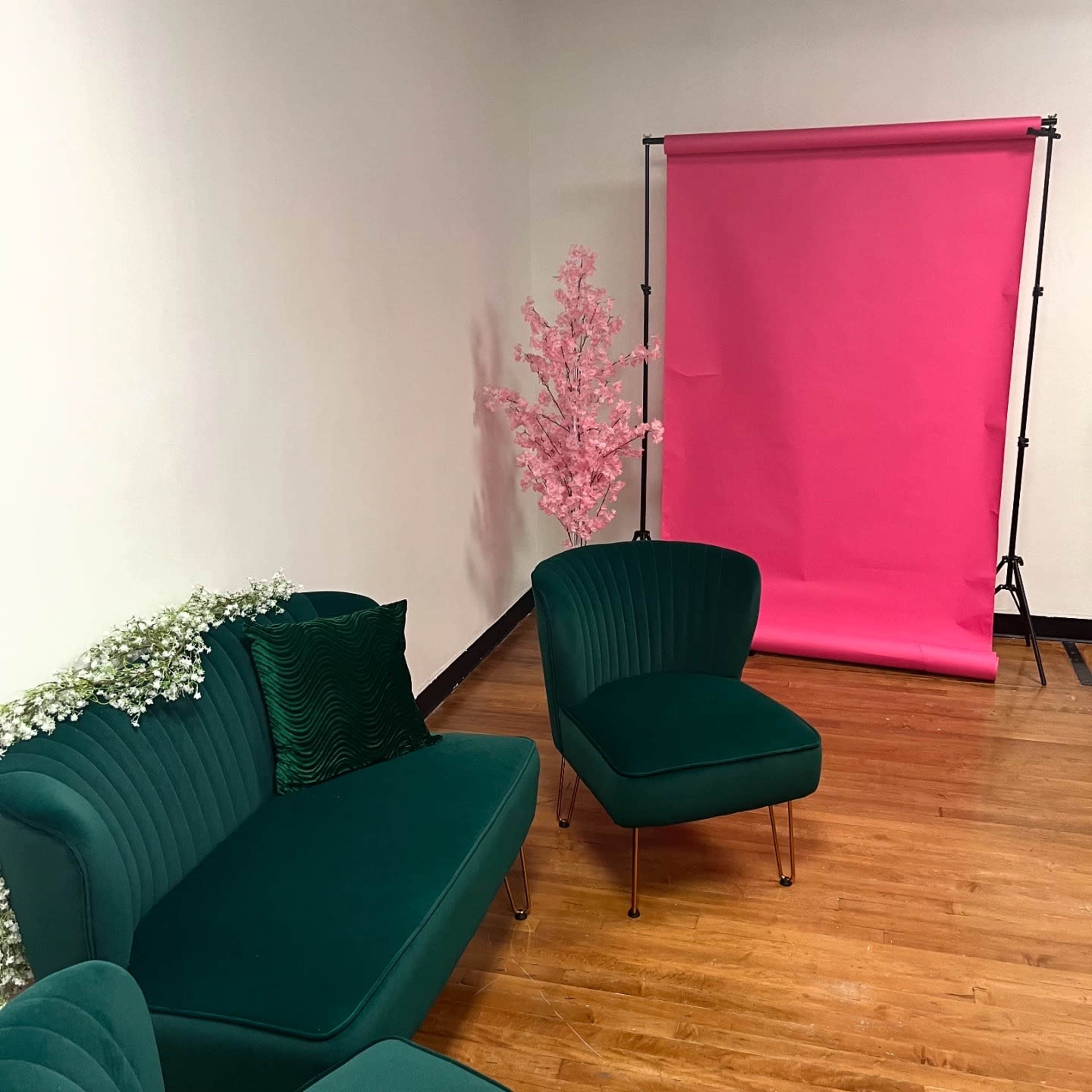 The image shows a small interior space featuring green chairs and a sofa, along with a pink backdrop and a decorative pink tree.