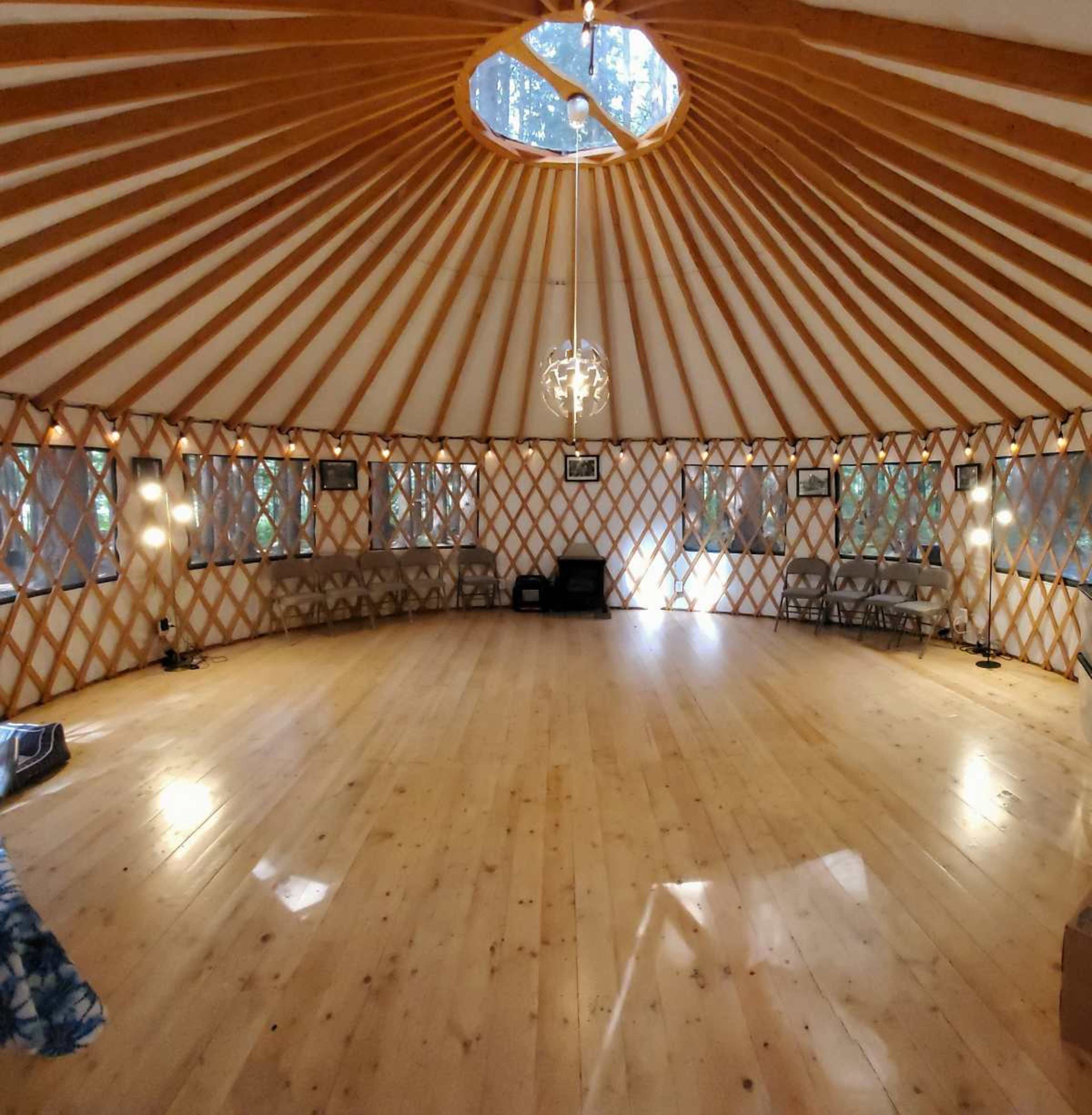 The image shows the interior of a yurt with wooden beams, a circular skylight, and wooden flooring.