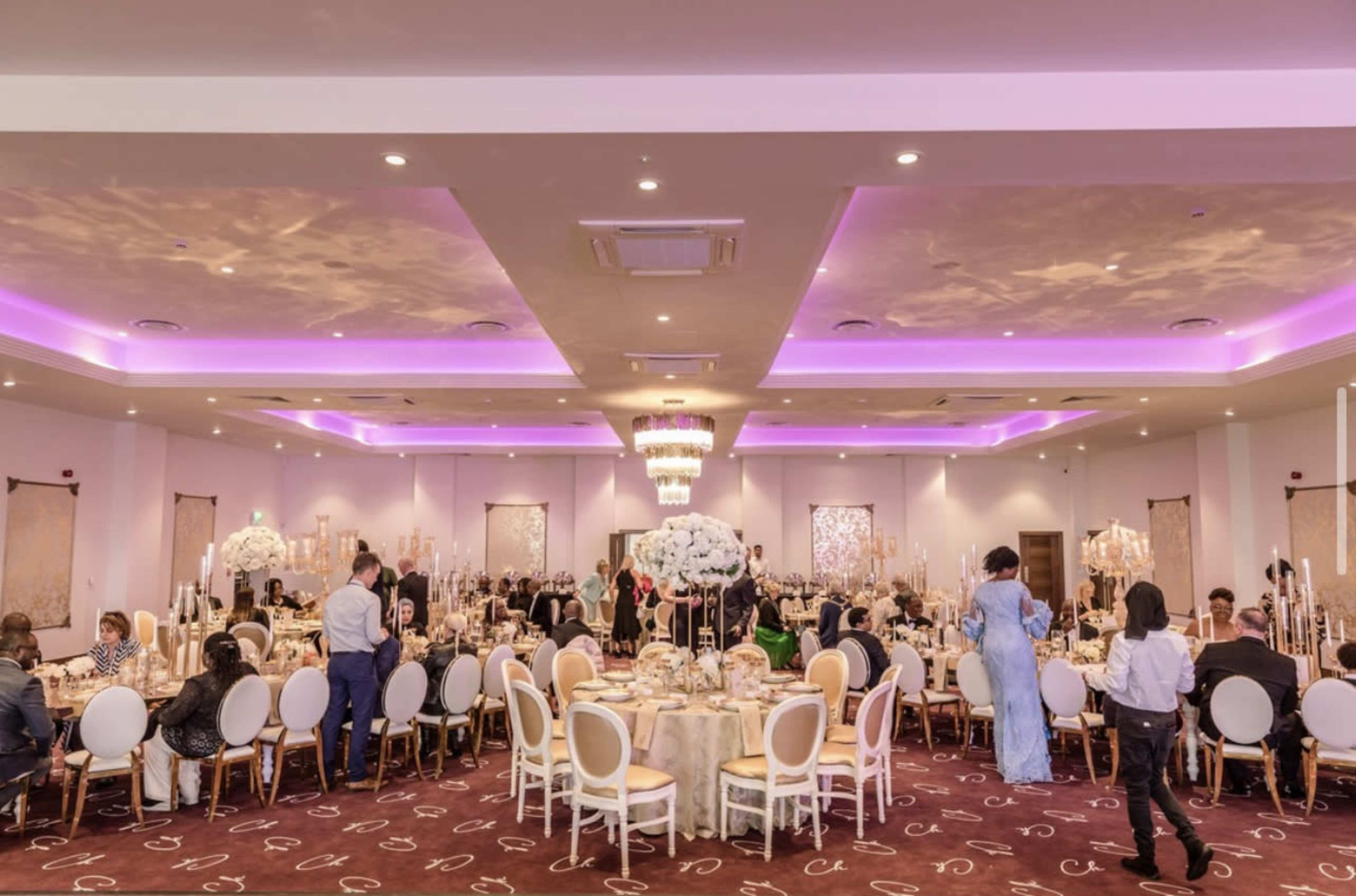 A large banquet hall is set up for a formal dinner, featuring round tables with elegant centerpieces and attendees dressed in formal attire.
