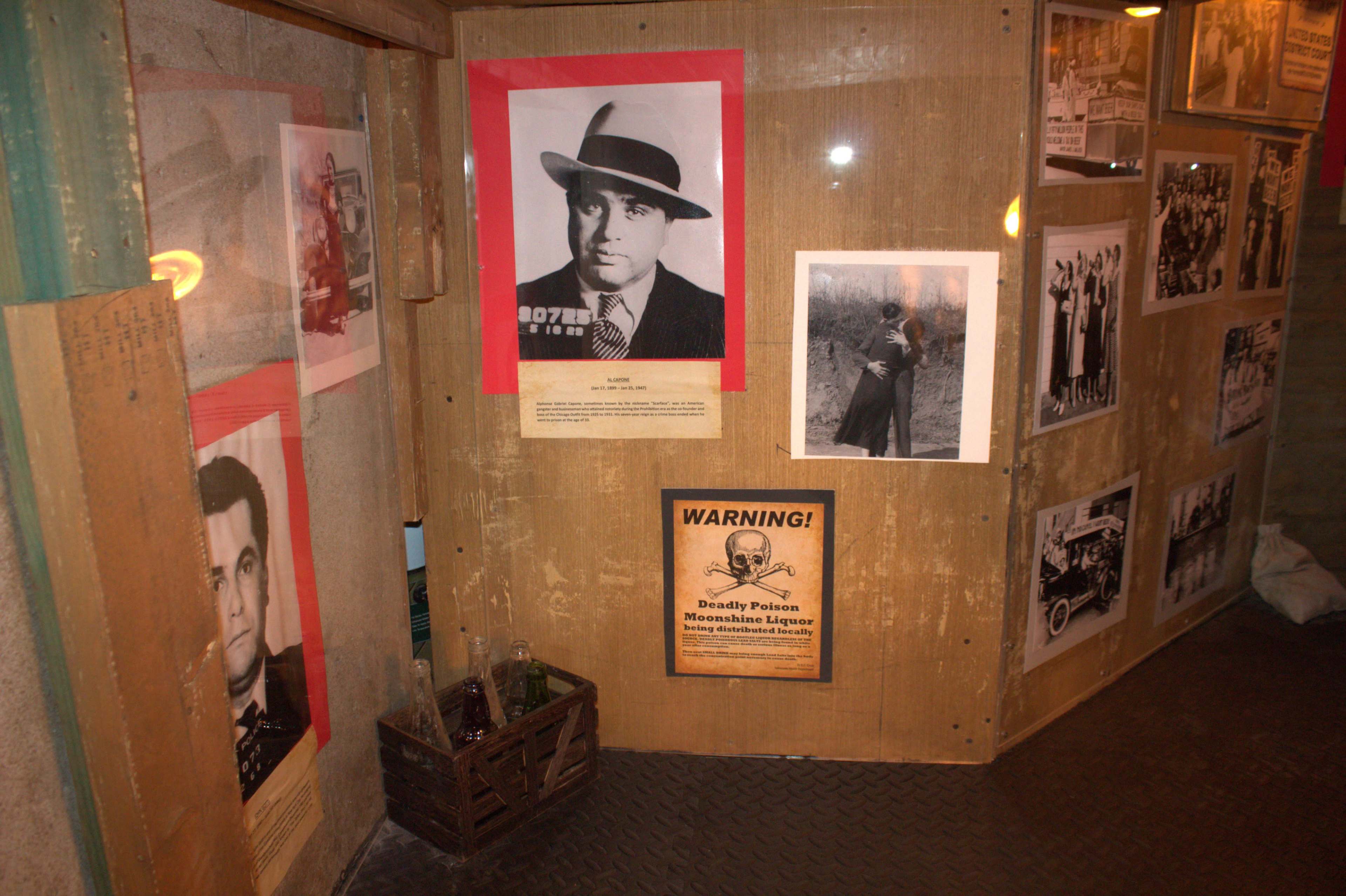 The image shows a wooden wall decorated with various black-and-white photographs and a warning sign, creating a historical display.
