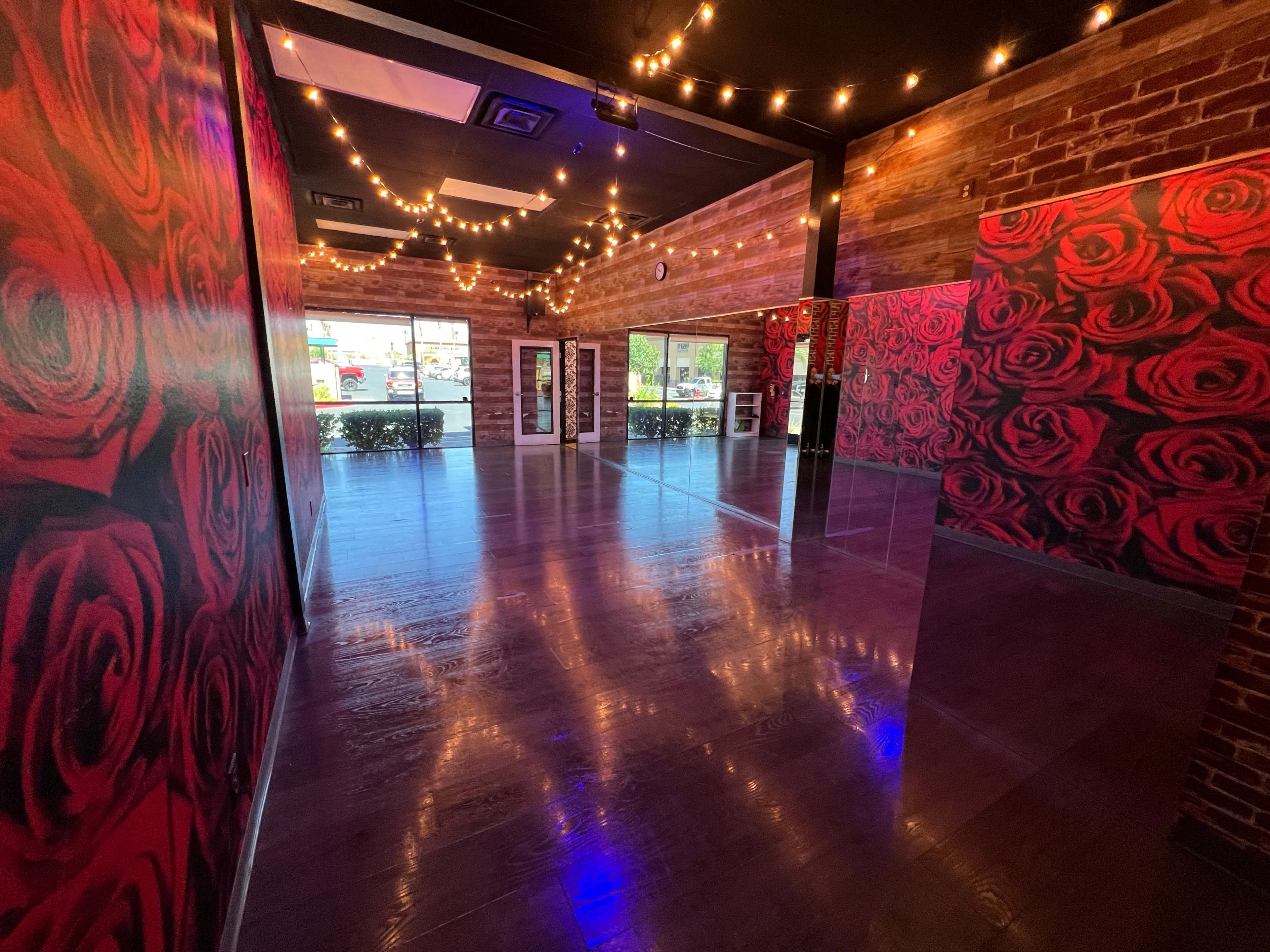 The image shows a room with brick walls adorned with rose-patterned wallpaper, wooden flooring, and string lights suspended from the ceiling.