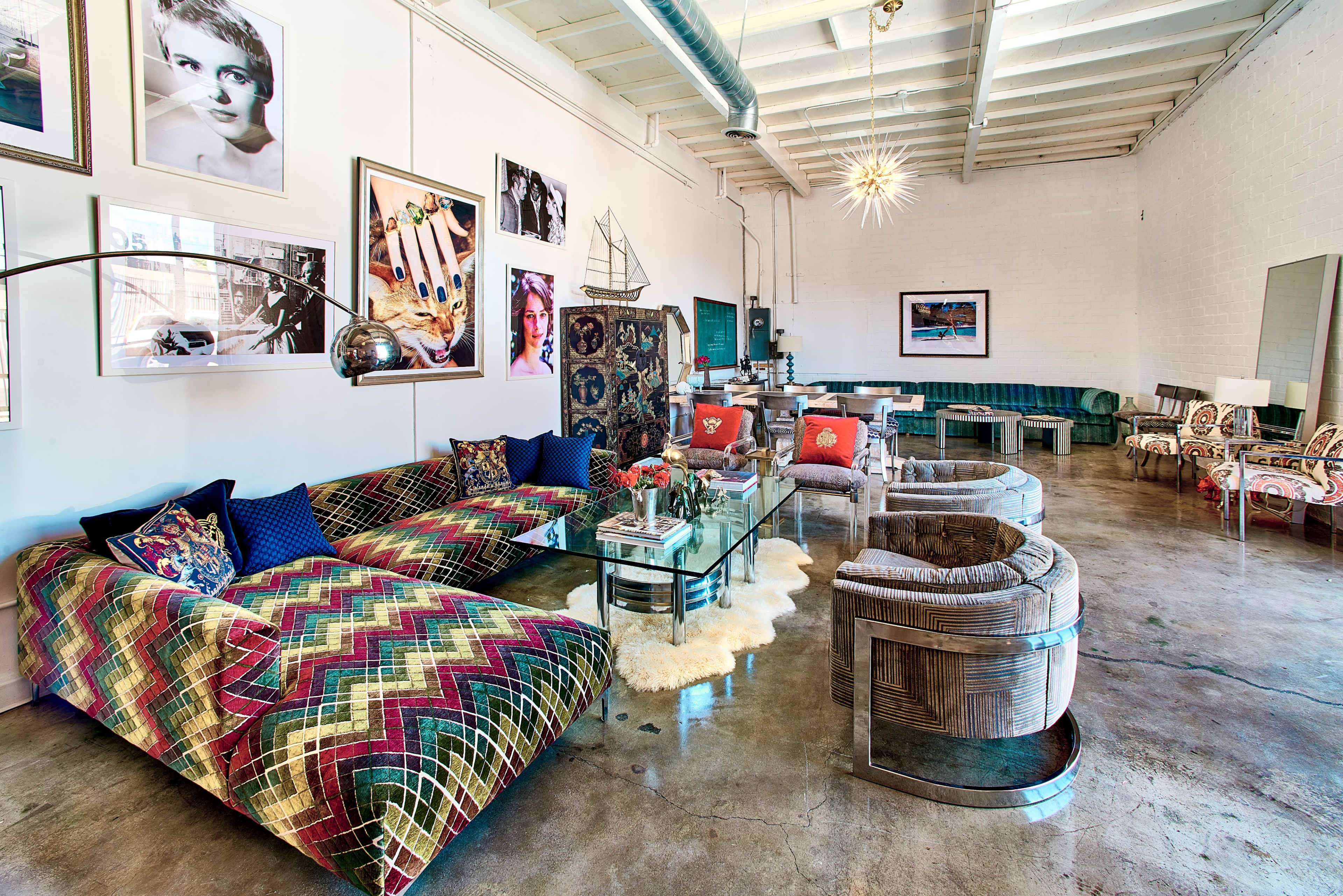 The image features a modern interior space with colorful patterned sofas, large artwork on the walls, and a mix of vintage and contemporary furniture.
