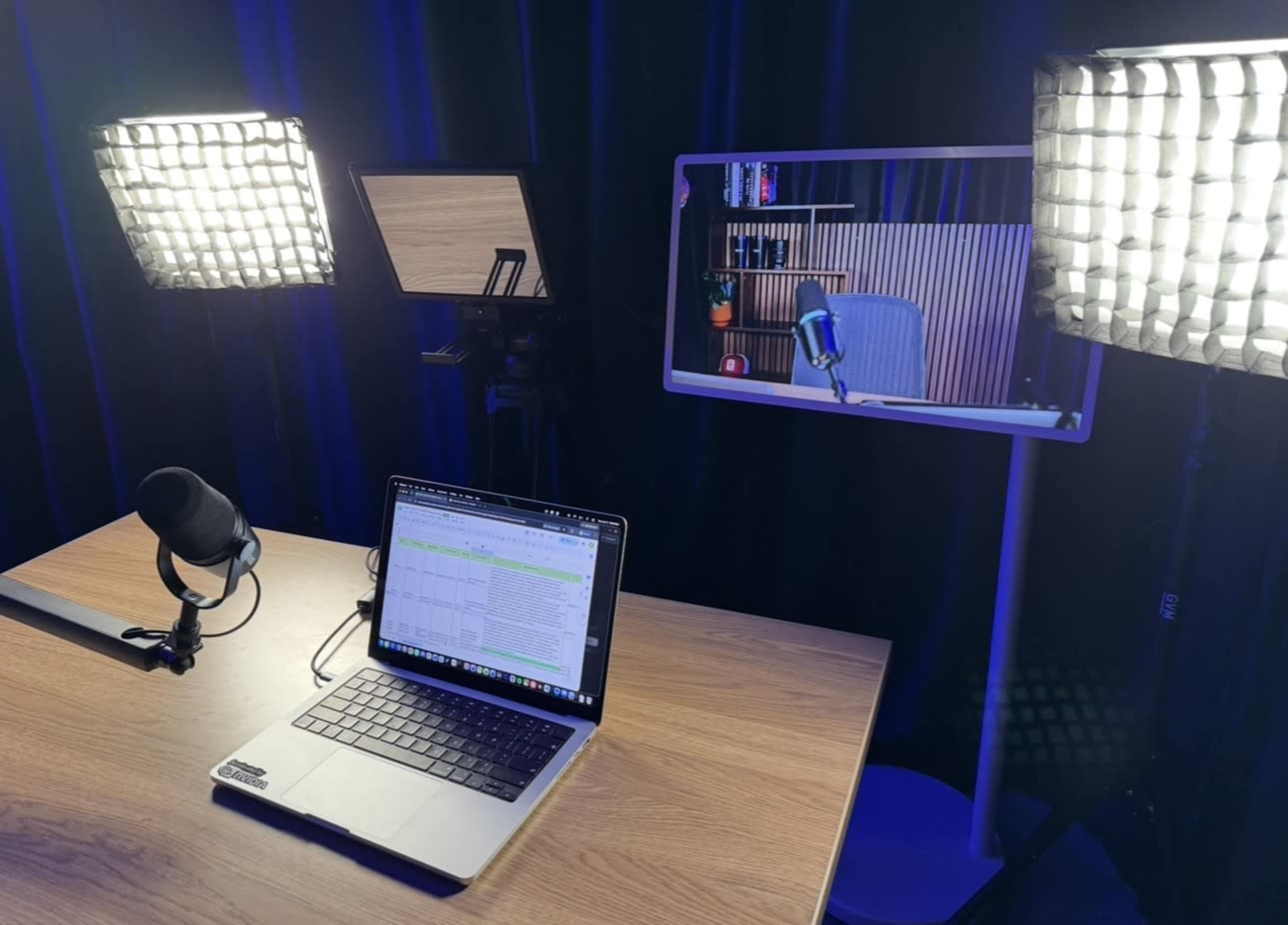 A well-lit podcast studio setup features a laptop with a spreadsheet, a microphone, and a mirror showing an empty chair against a wooden backdrop.