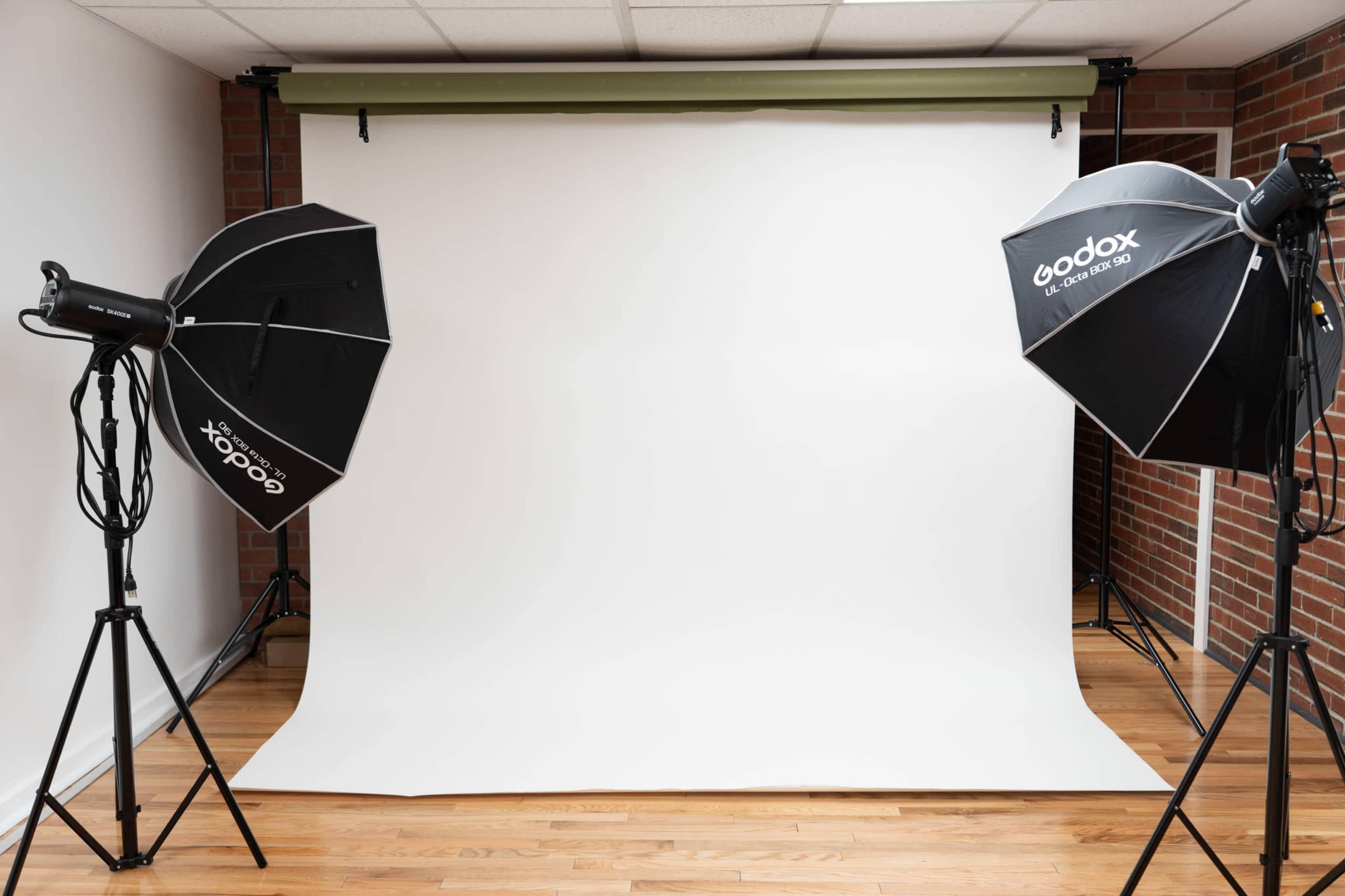 A photography studio is set up with two softbox lights positioned on either side of a plain white backdrop.