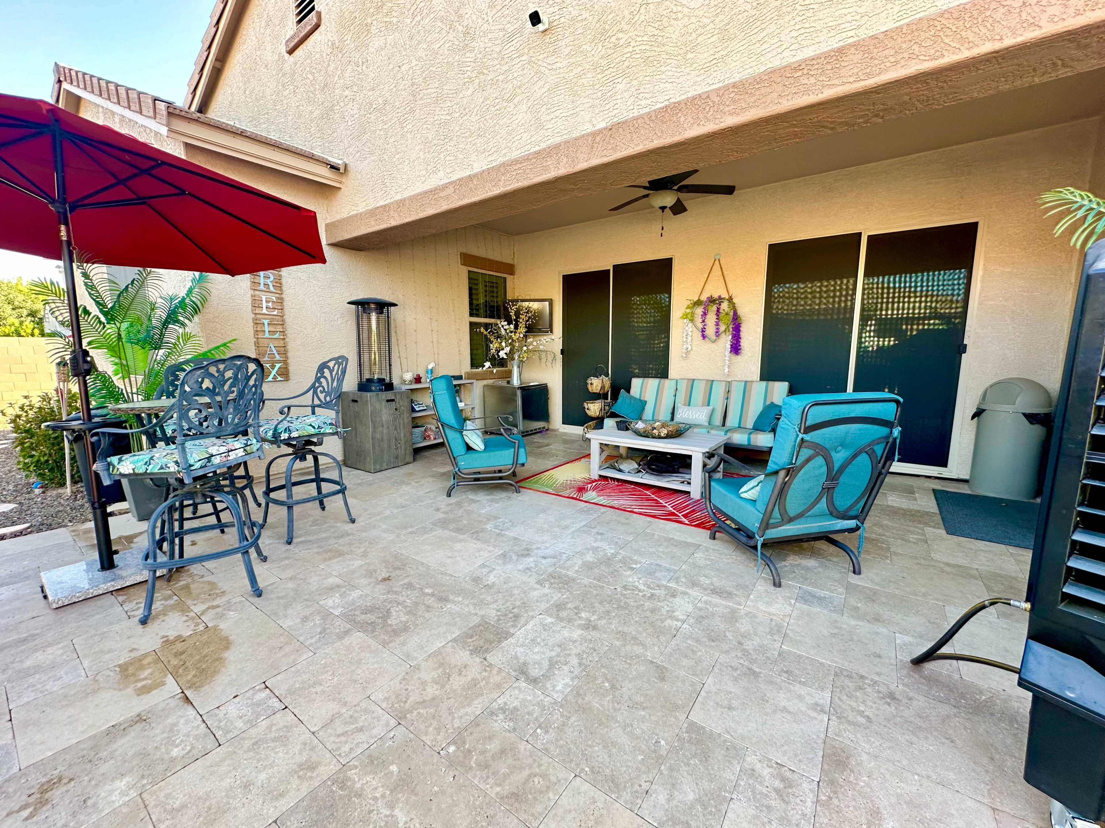 A patio area featuring a table with chairs, a couch set, a red umbrella, and a decorative rug.