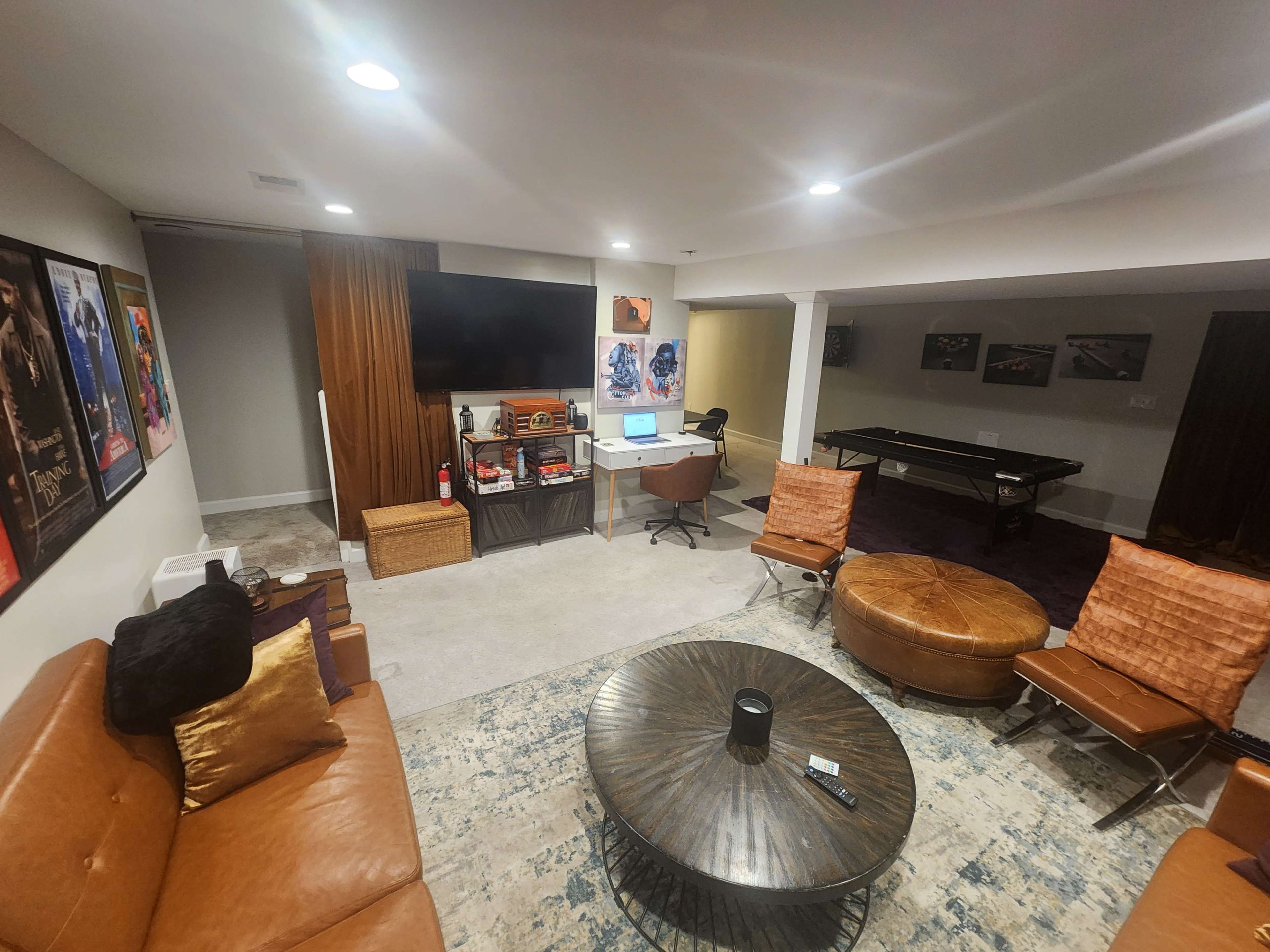 A modern basement recreational area features a seating arrangement with brown leather furniture, a pool table, and a wall-mounted television.
