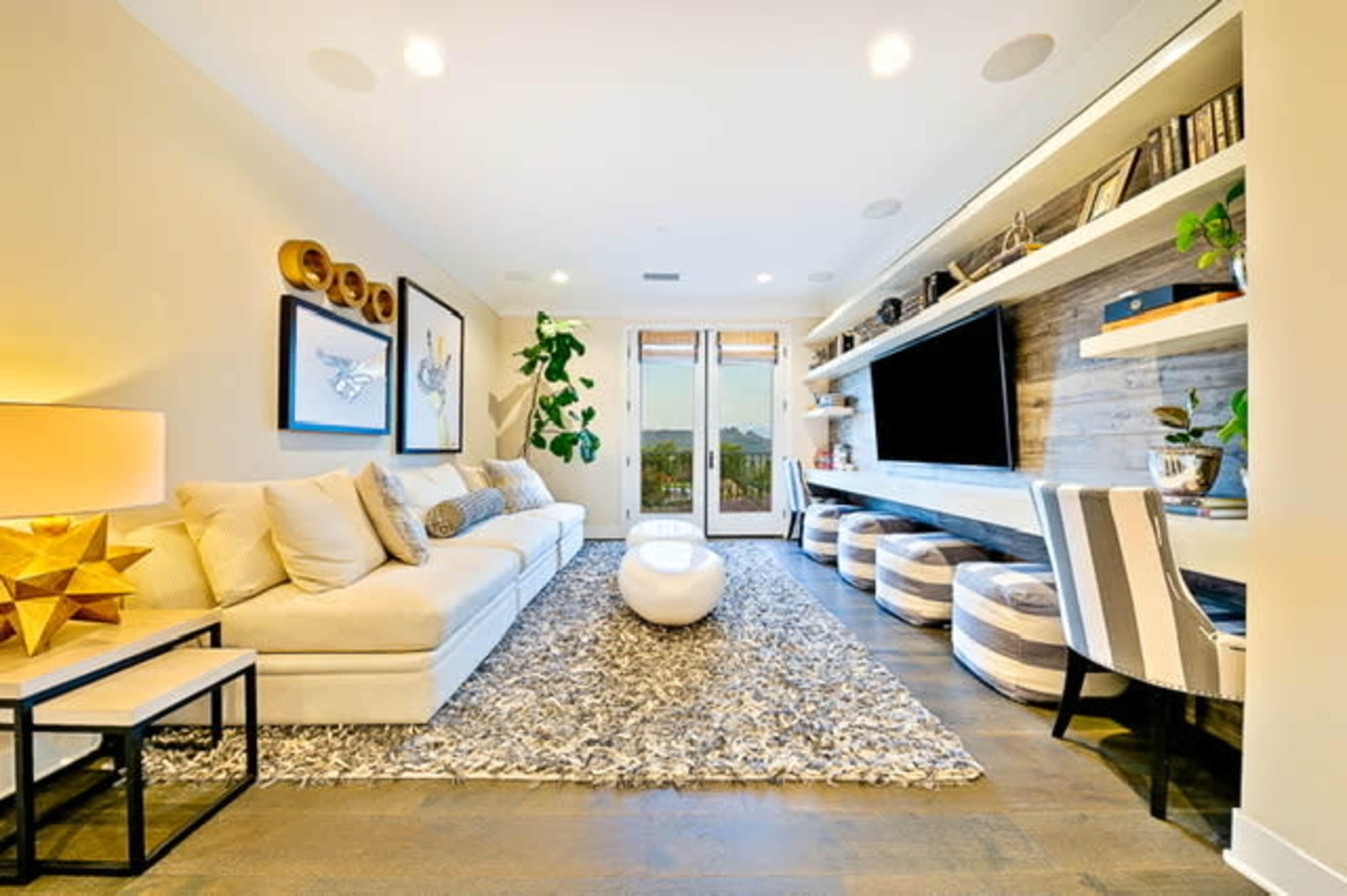 A modern living room with a large sectional sofa, a round coffee table, a wall-mounted TV, and built-in shelves, complemented by a textured area rug.