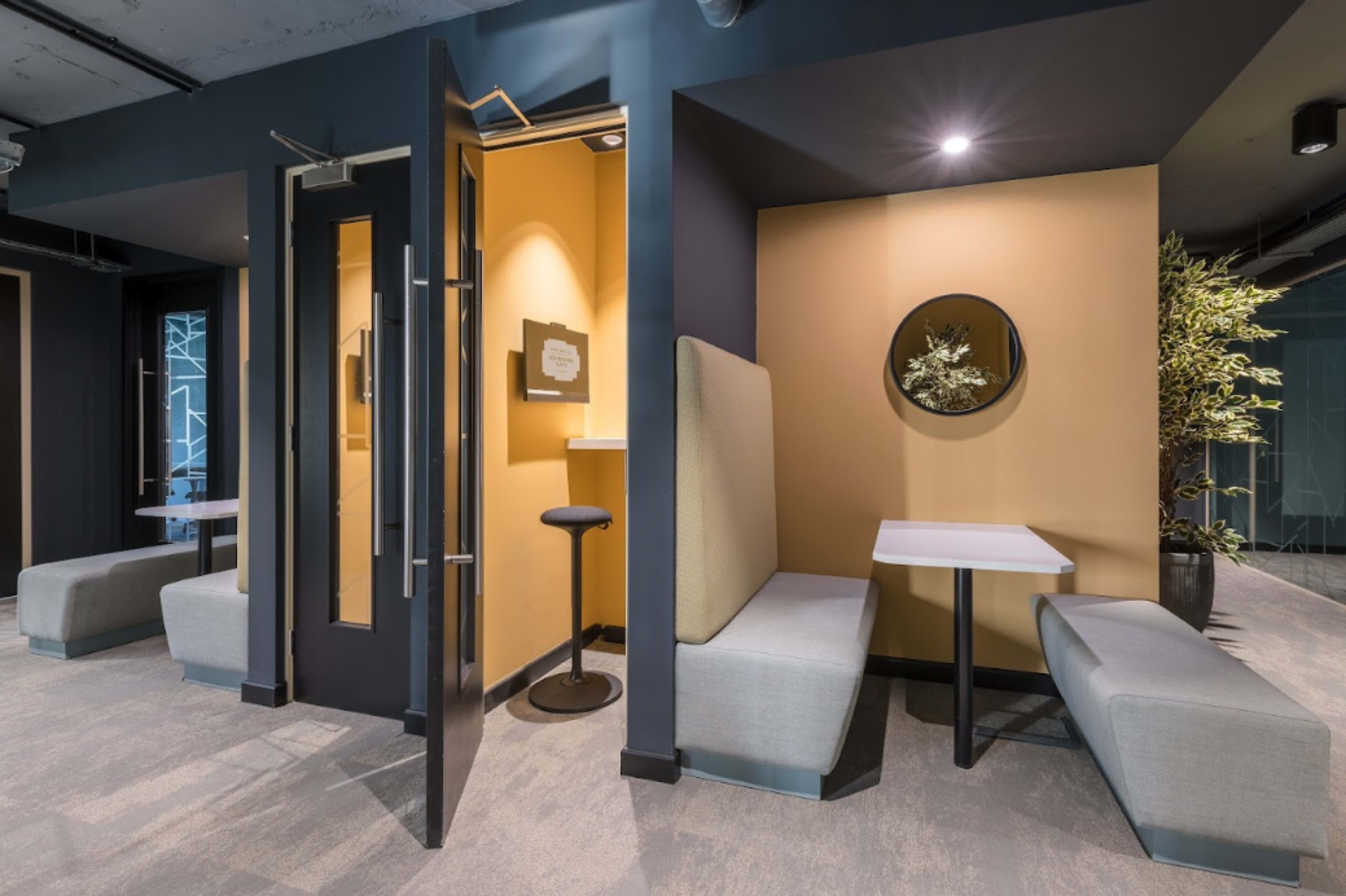 A modern interior space with a small seating area featuring benches, a round mirror, and a standing table.