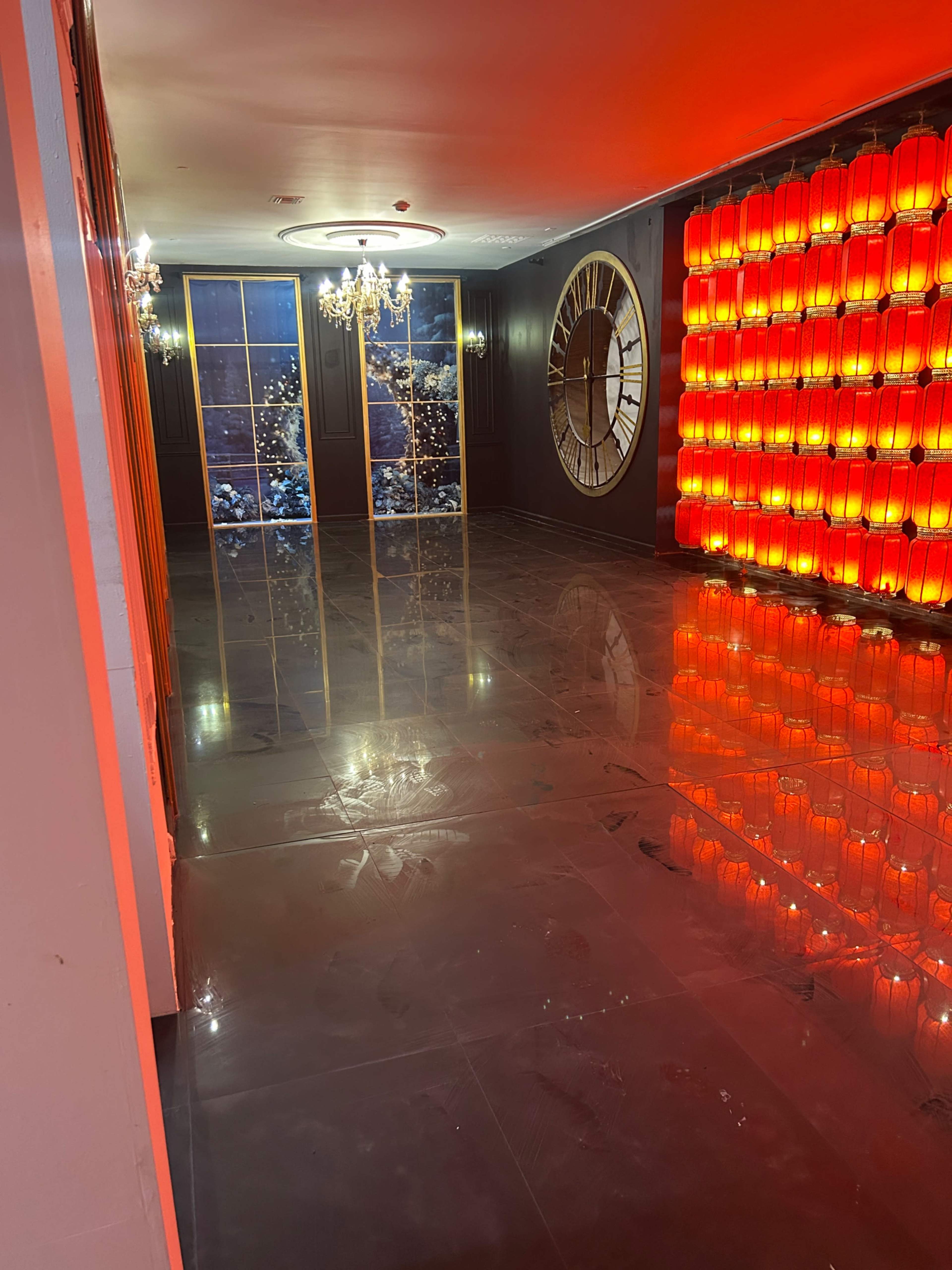 The image shows a modern room with a large wall featuring illuminated red lanterns, a round clock, and a shiny floor reflecting the bright lighting.