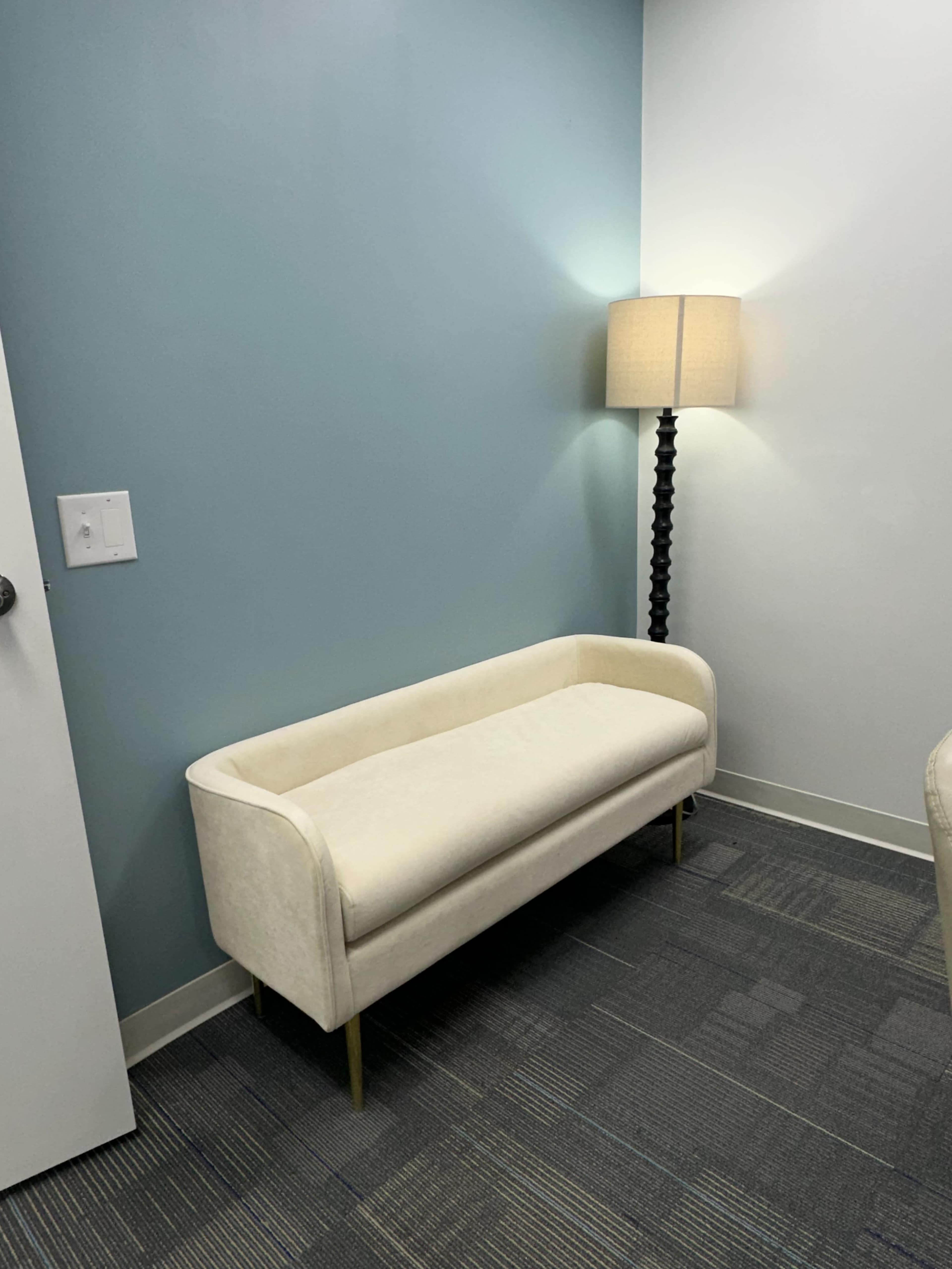 A small, cream-colored couch against a light blue wall, next to a floor lamp.