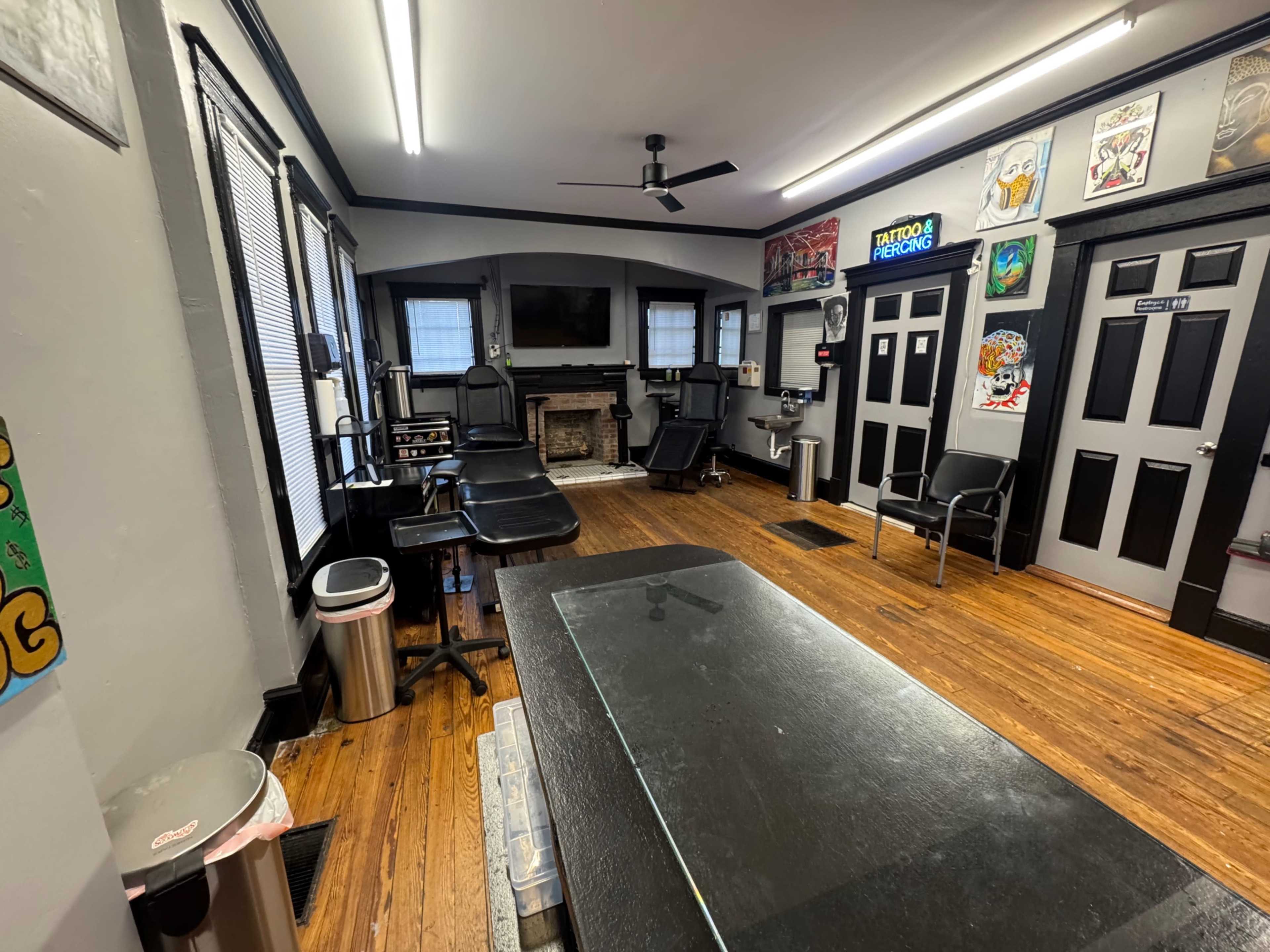 The image shows the interior of a tattoo studio featuring several tattoo chairs, a reception area with a countertop, and decorated walls with artwork.