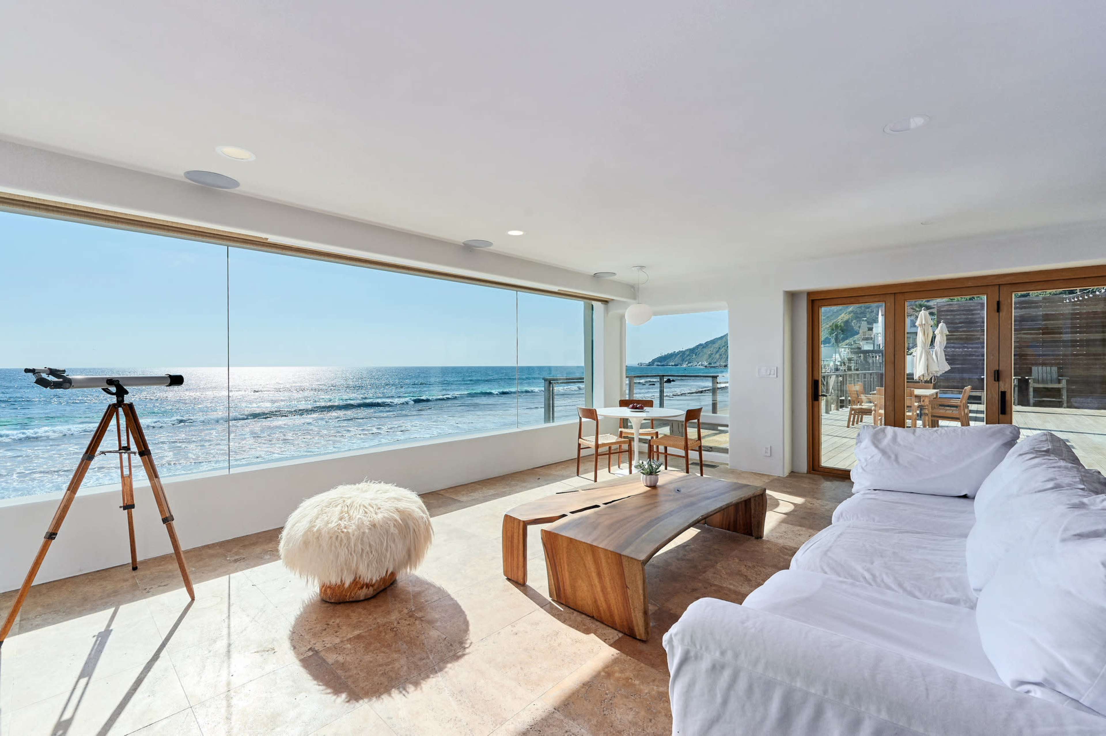 A spacious living room features a large glass window overlooking the ocean, a telescope, and modern furniture.