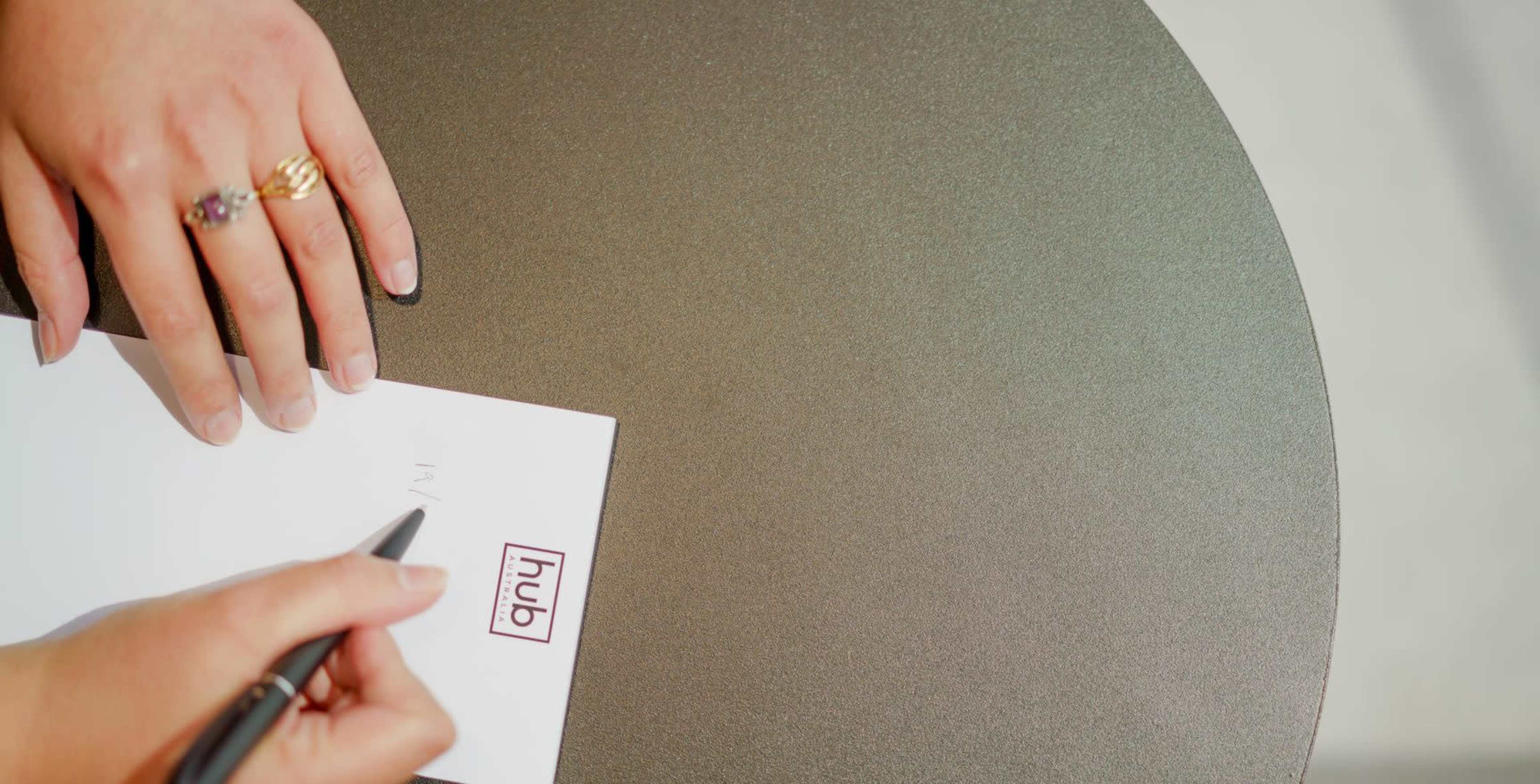 A person's hands are writing on a piece of paper placed on a round table with the word "hub" printed on it.