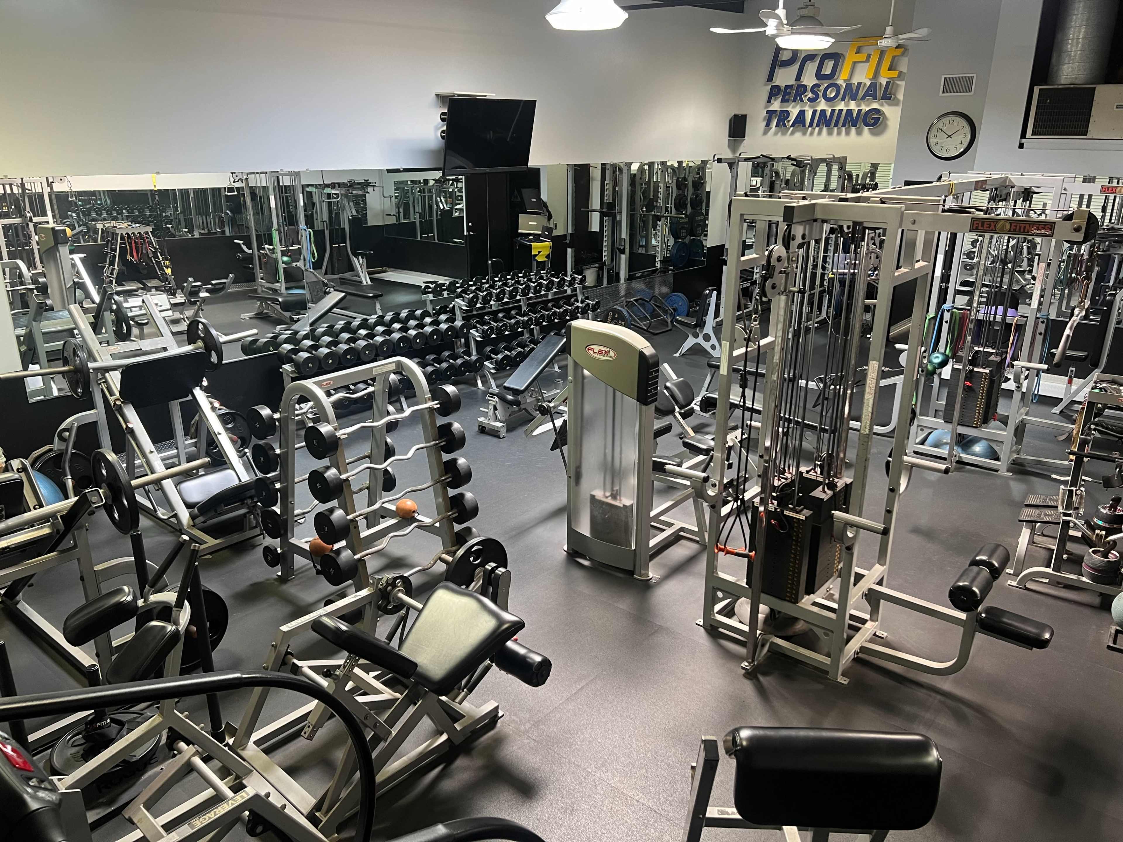 The image shows a well-equipped gym with various exercise machines, free weights, and mirrors.