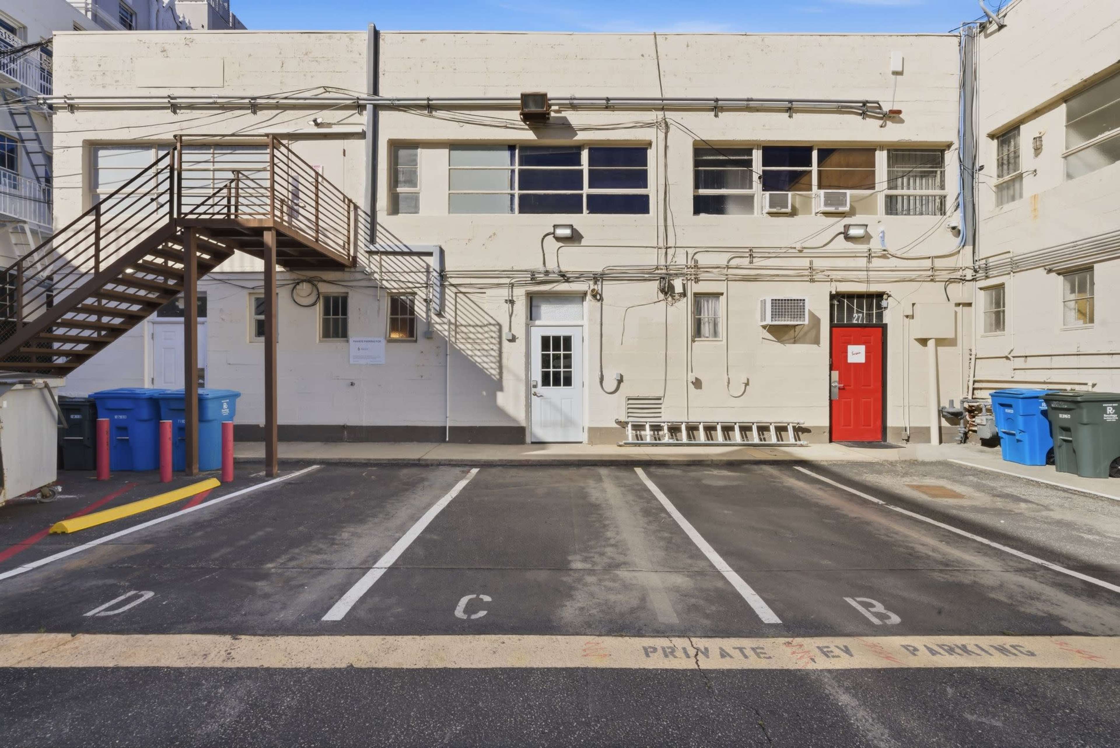 The image shows a parking area with marked spaces labeled A, B, C, and D, alongside a building featuring a staircase and a red door.
