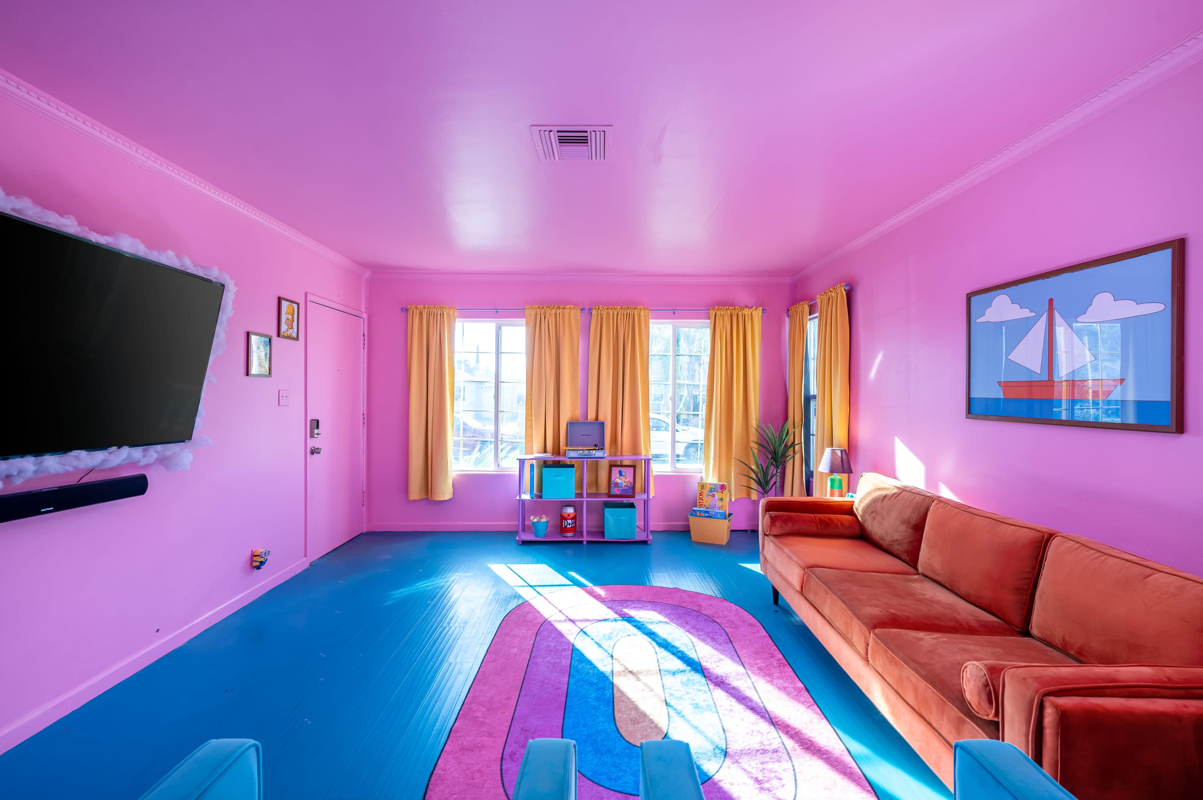A living room features pink walls, a blue floor, a brown couch, and large windows with yellow curtains.