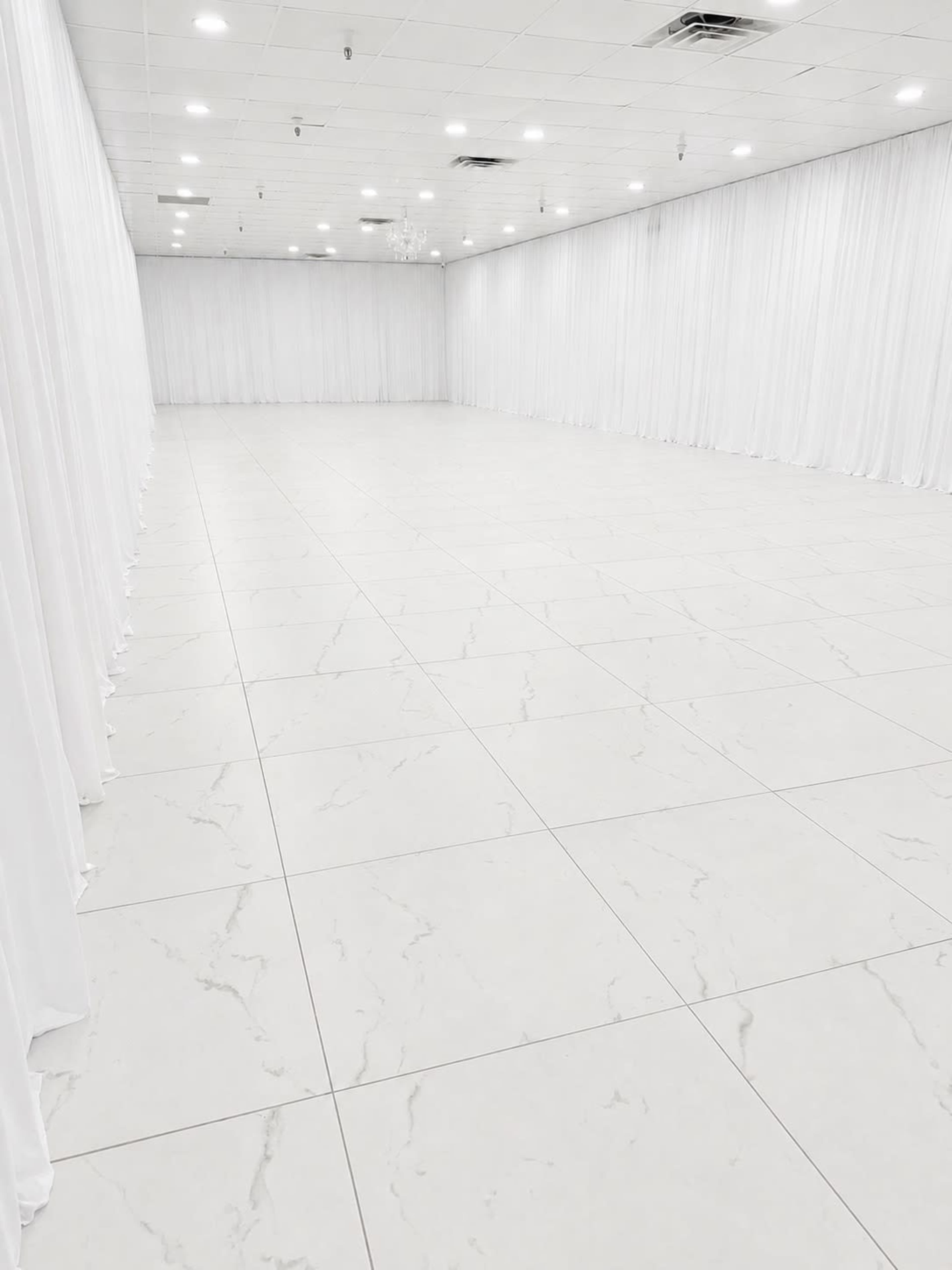 The image shows a spacious, empty room with white marble flooring and white drapery along the walls.