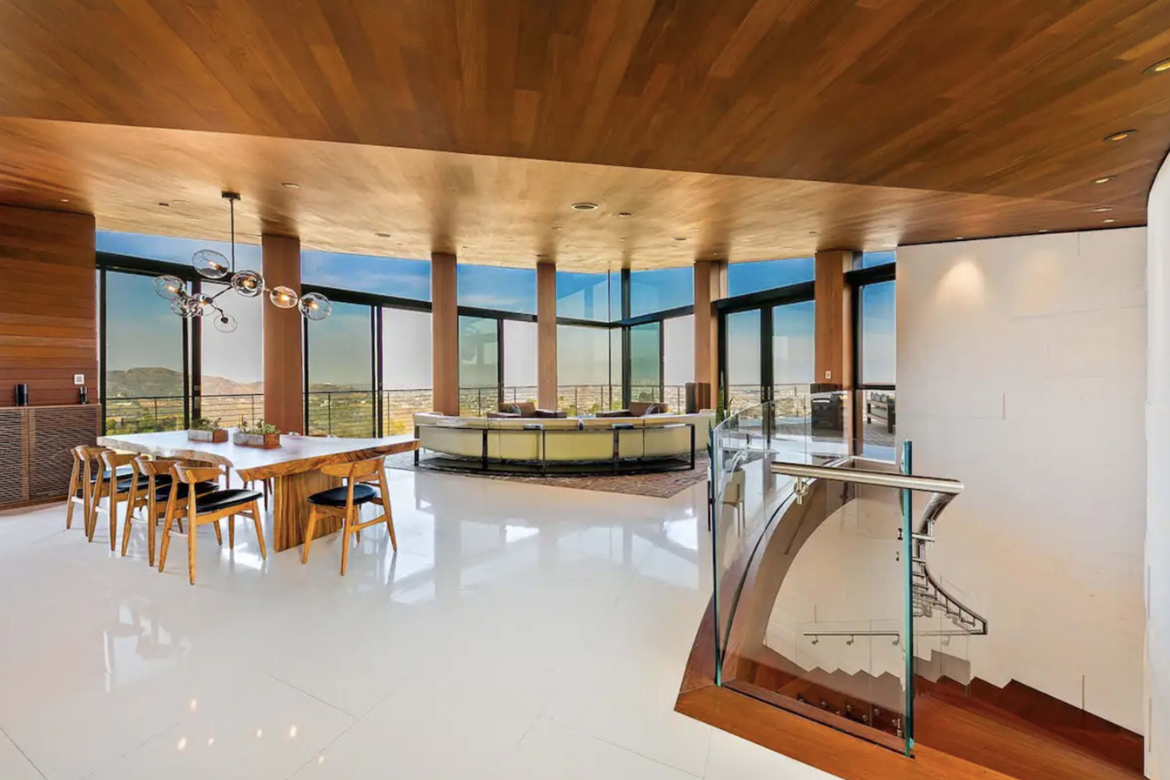 A modern interior space with a dining area, a lounge area with large windows, and a staircase leading down to another level.