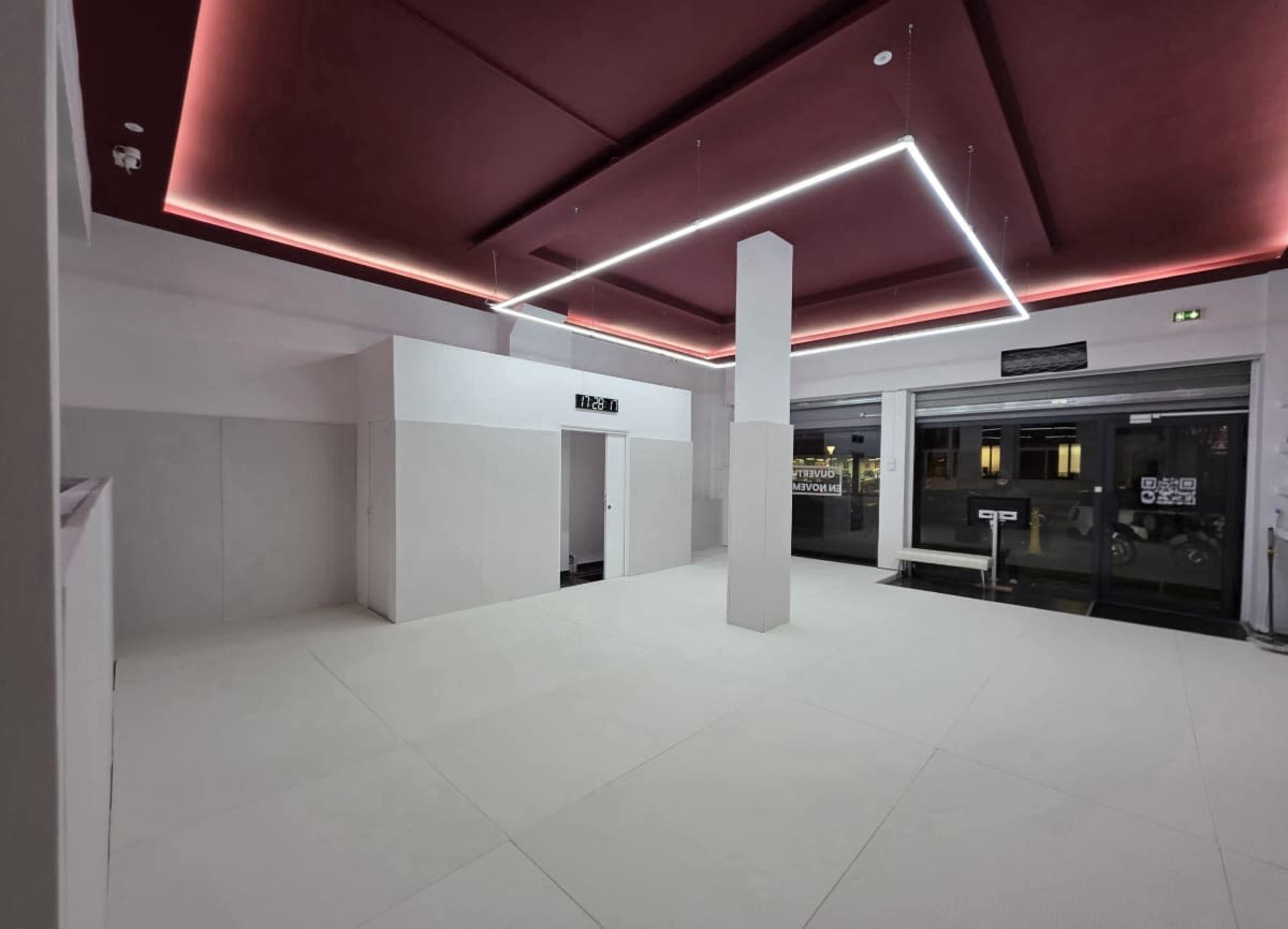 The image shows an empty, spacious interior with a stark white floor and walls, highlighted by a red ceiling and modern lighting.