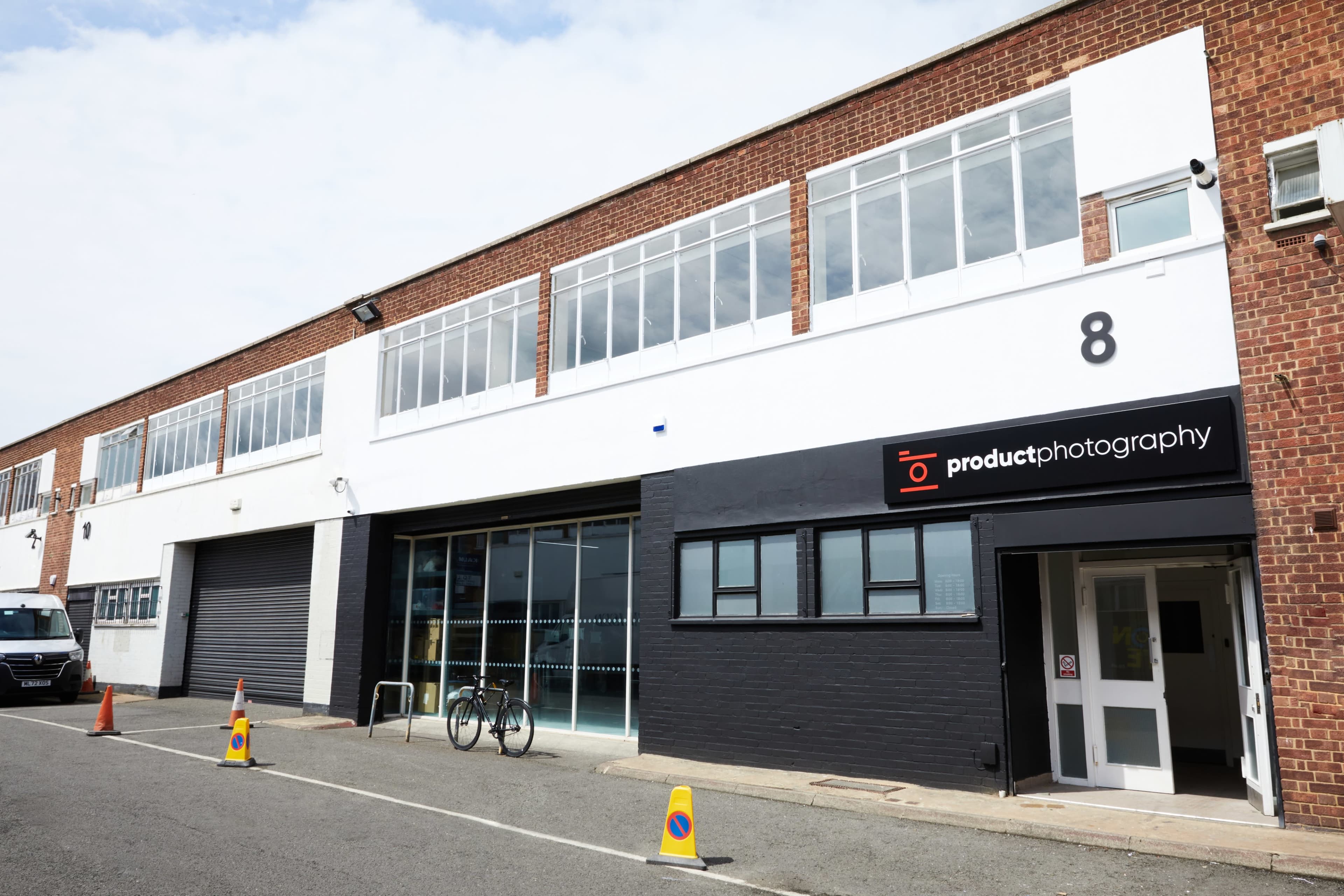 The image shows a commercial building with a large white storefront labeled "productphotography," flanked by windows and featuring a bicycle parked outside.