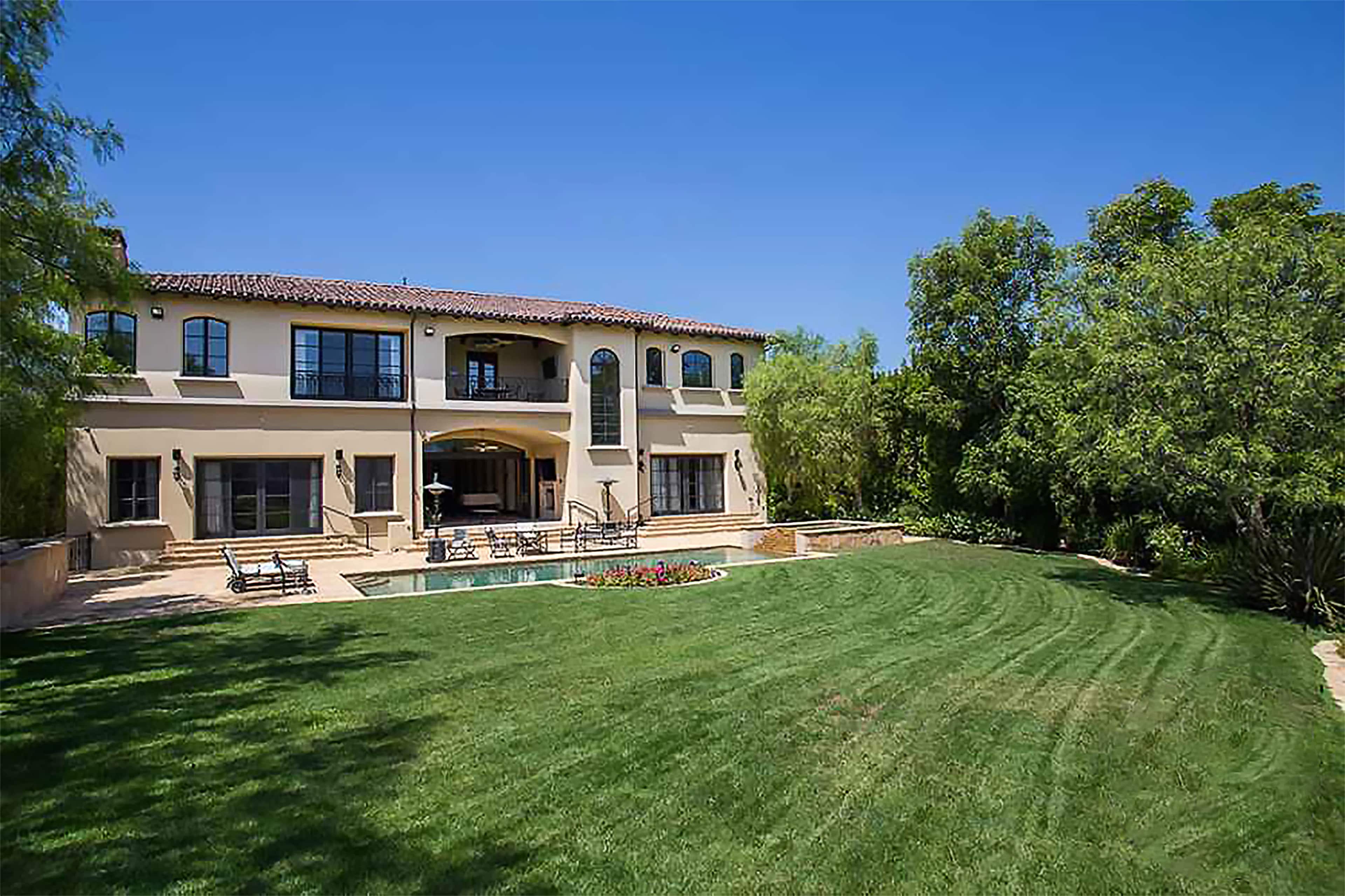 A two-story house with a tile roof overlooks a landscaped yard featuring a pool and patio area.