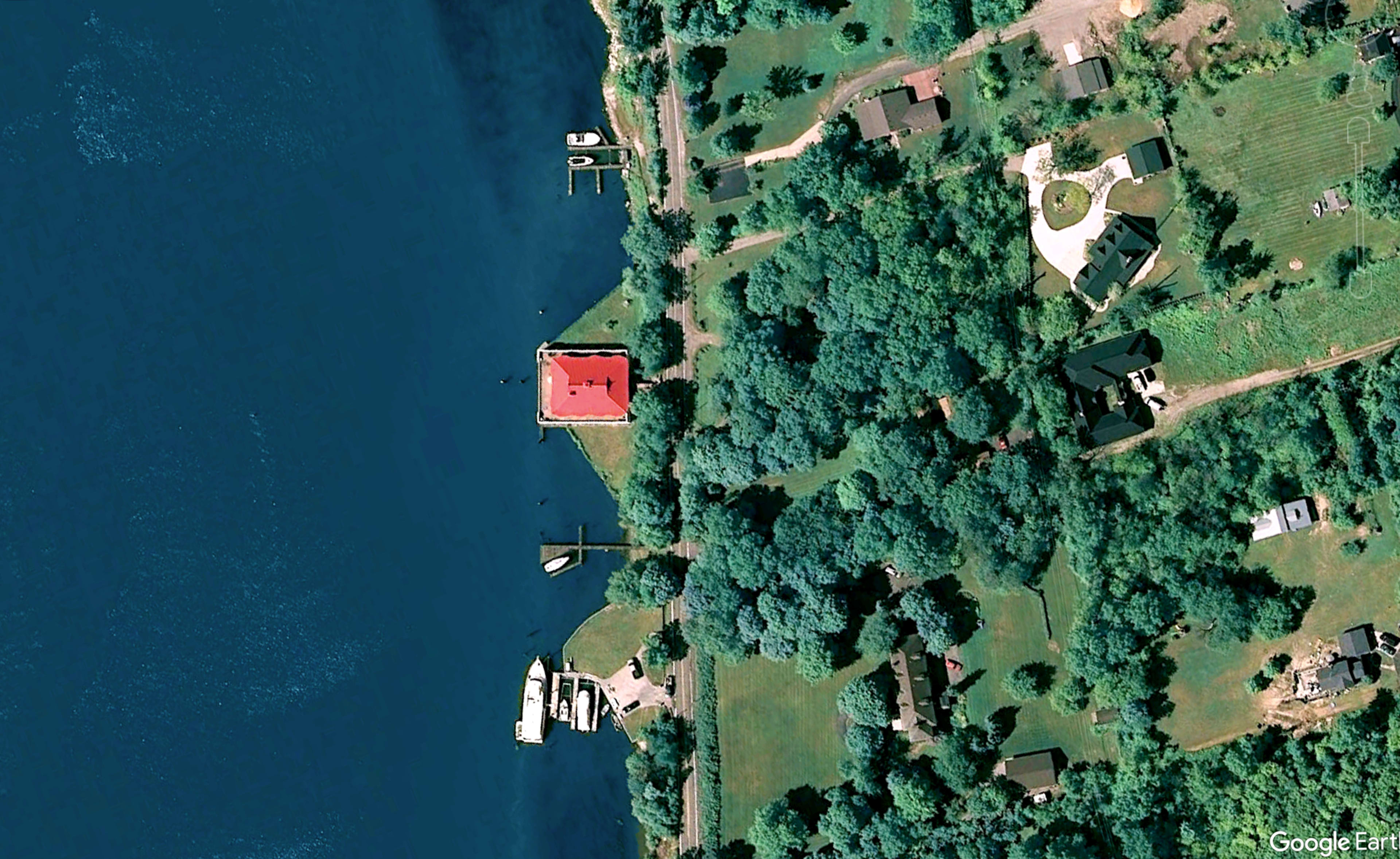 The image shows a satellite view of a lakeside area with several houses, a red-roofed structure, and pathways leading to the water.