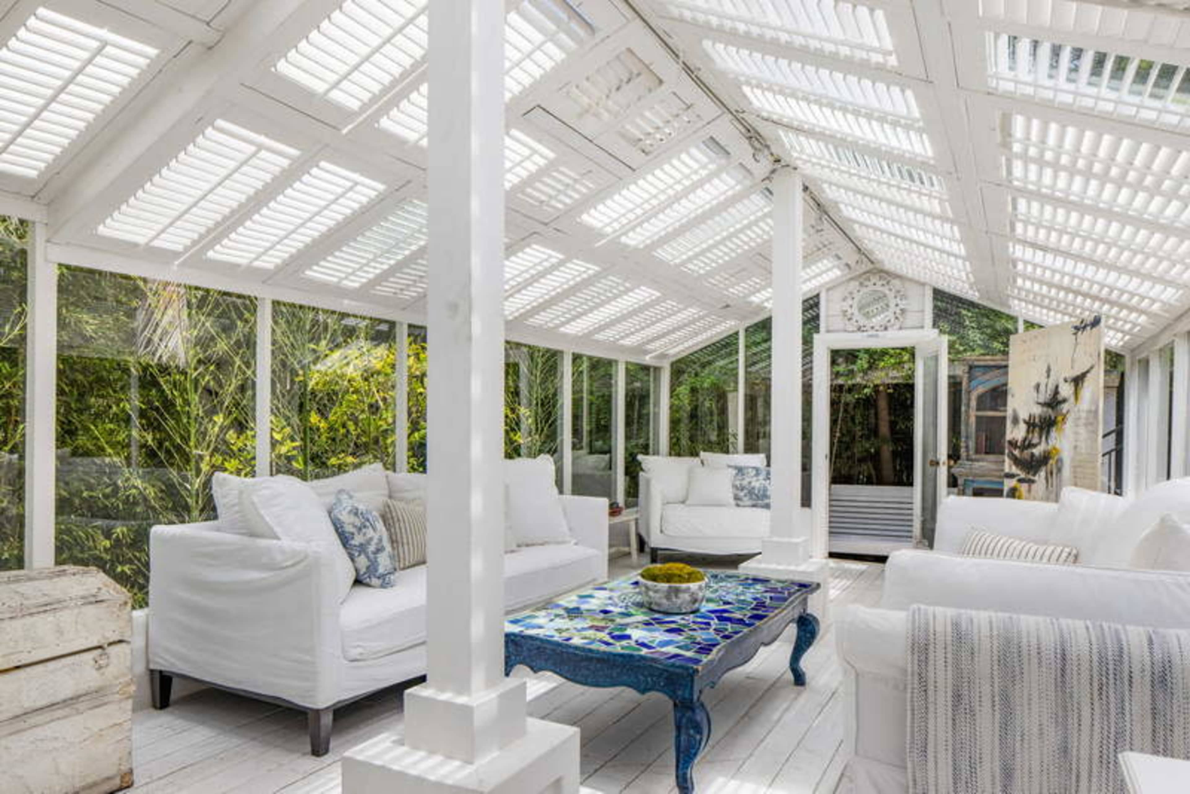 A bright sunroom filled with white seating, a colorful mosaic coffee table, and large windows allowing plenty of natural light.