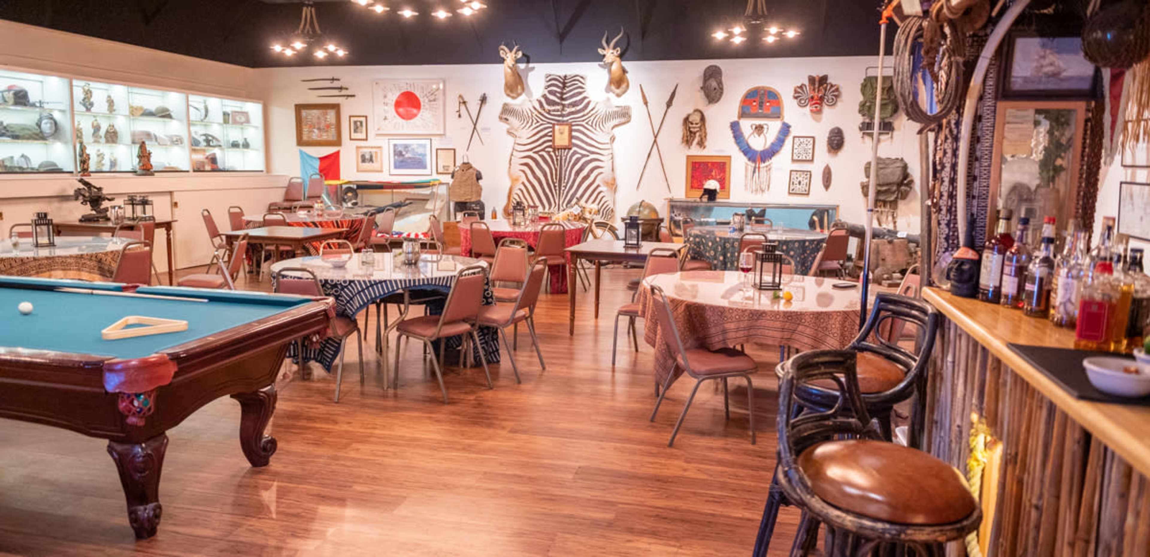 A restaurant interior featuring several tables, a pool table, and walls adorned with animal mounts and various artifacts.