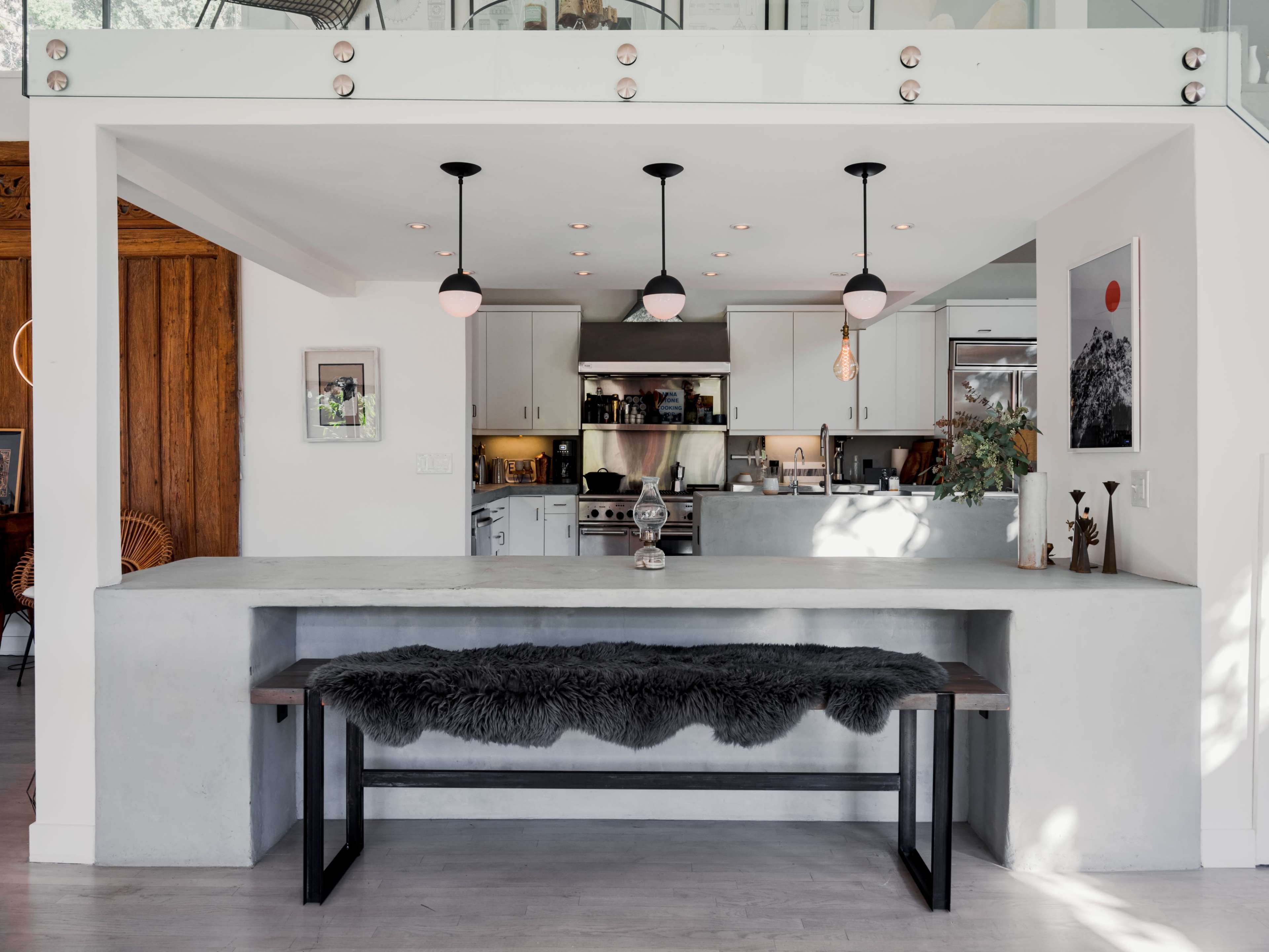A modern kitchen with a concrete bar and a long bench covered in faux fur, featuring pendant lights hanging overhead.