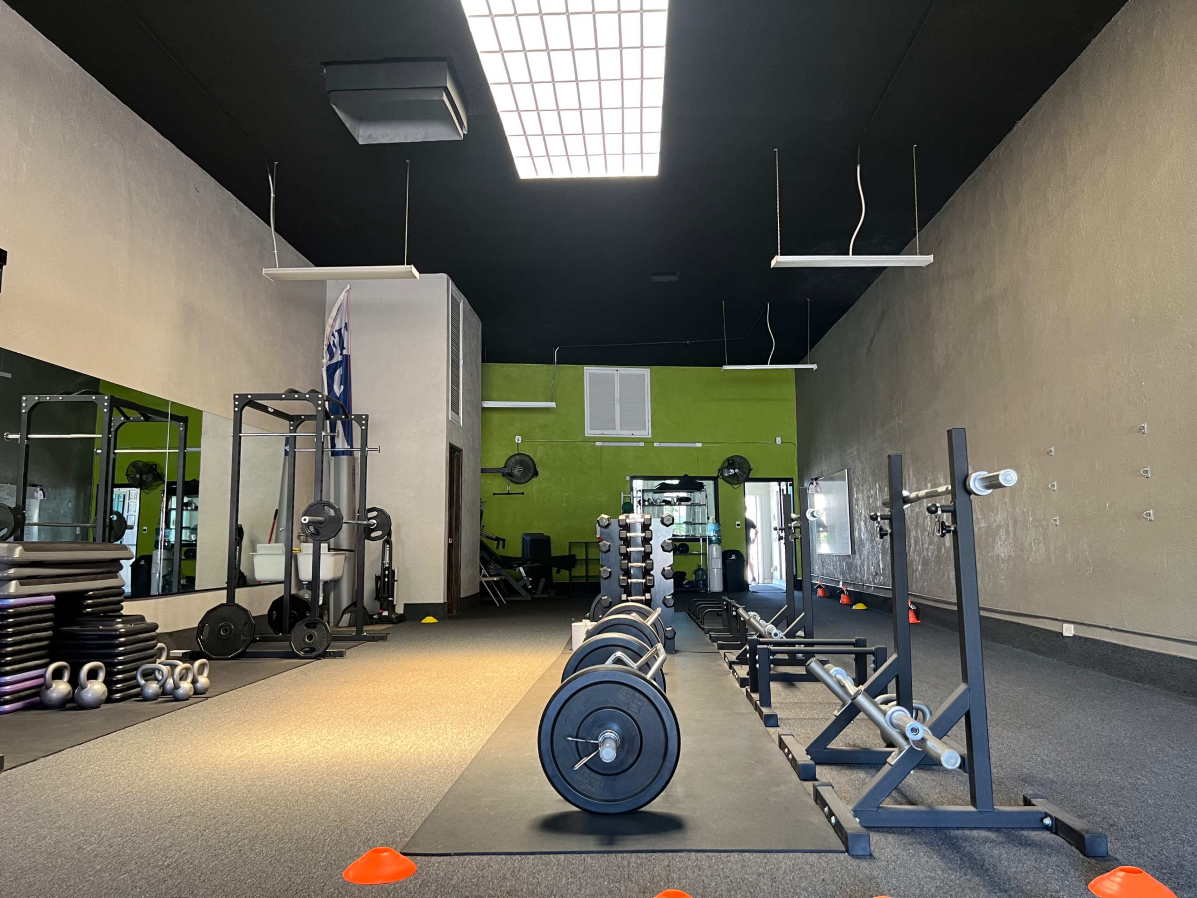 The image shows a spacious gym with exercise equipment neatly arranged, featuring dumbbells, benches, and mats on the floor.