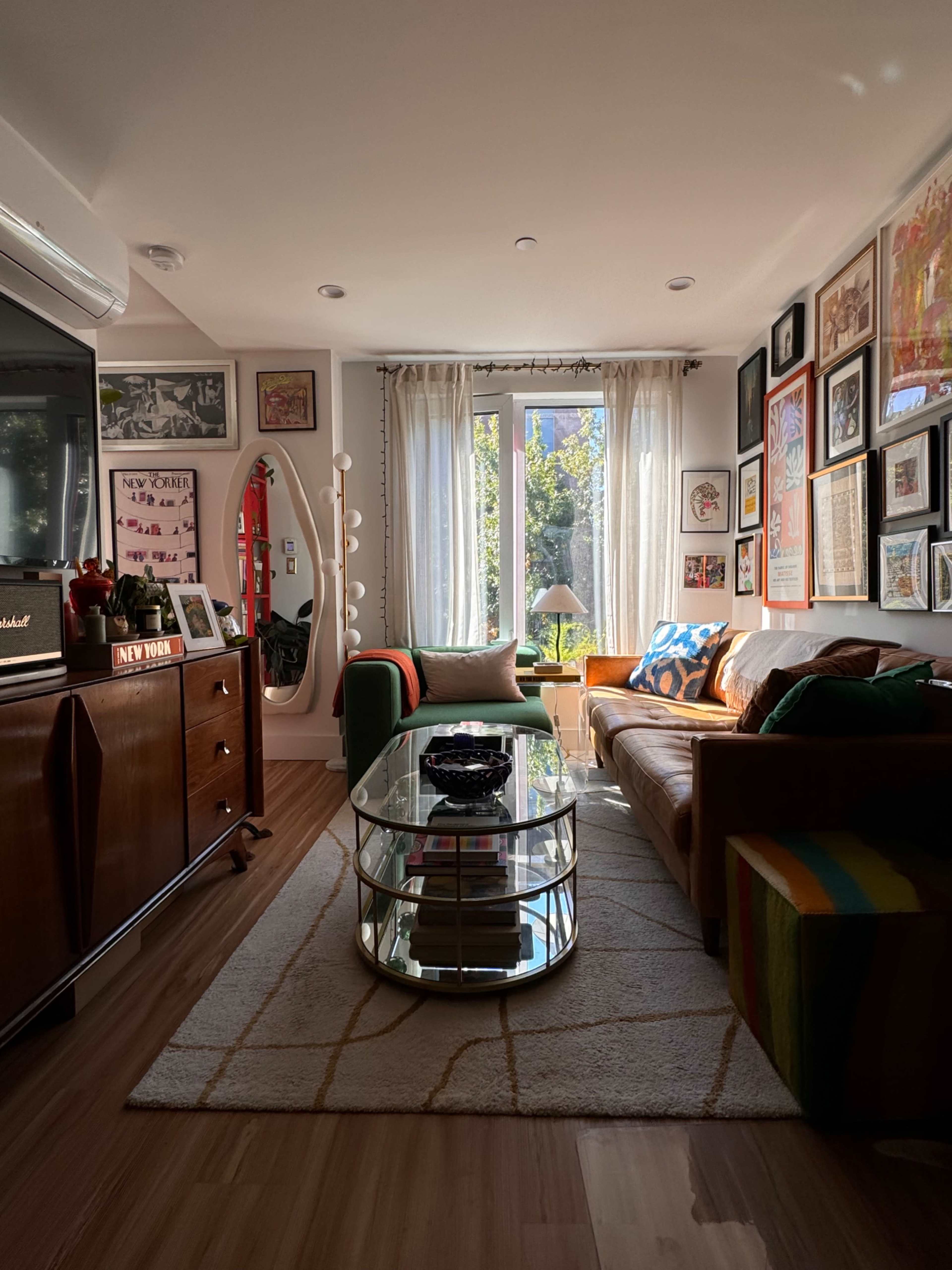 A cozy living room features a brown leather sofa, a glass coffee table, and walls adorned with various framed artworks.