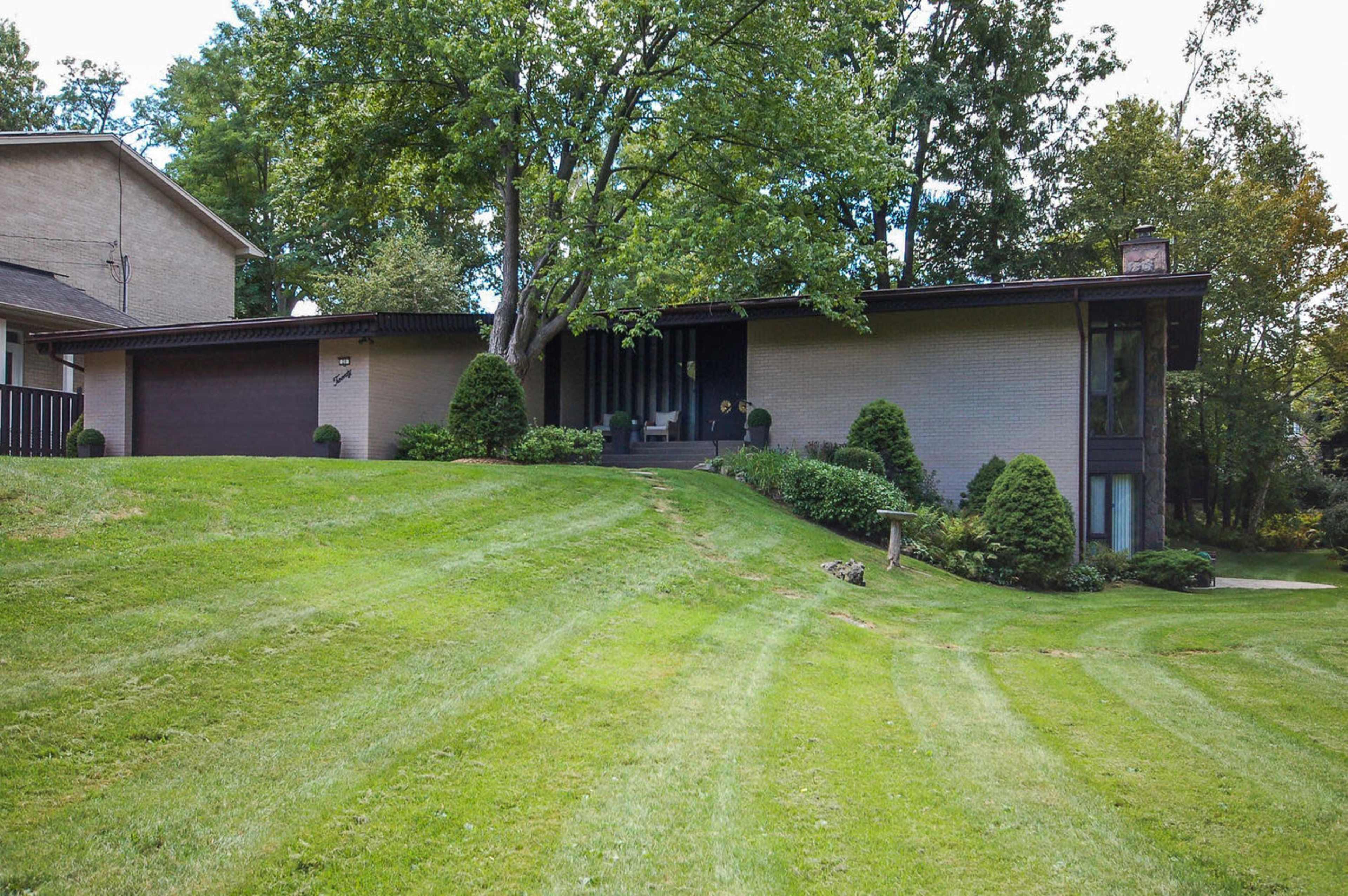 A modern-style home with a landscaped yard and a sloped lawn, set against a backdrop of trees.